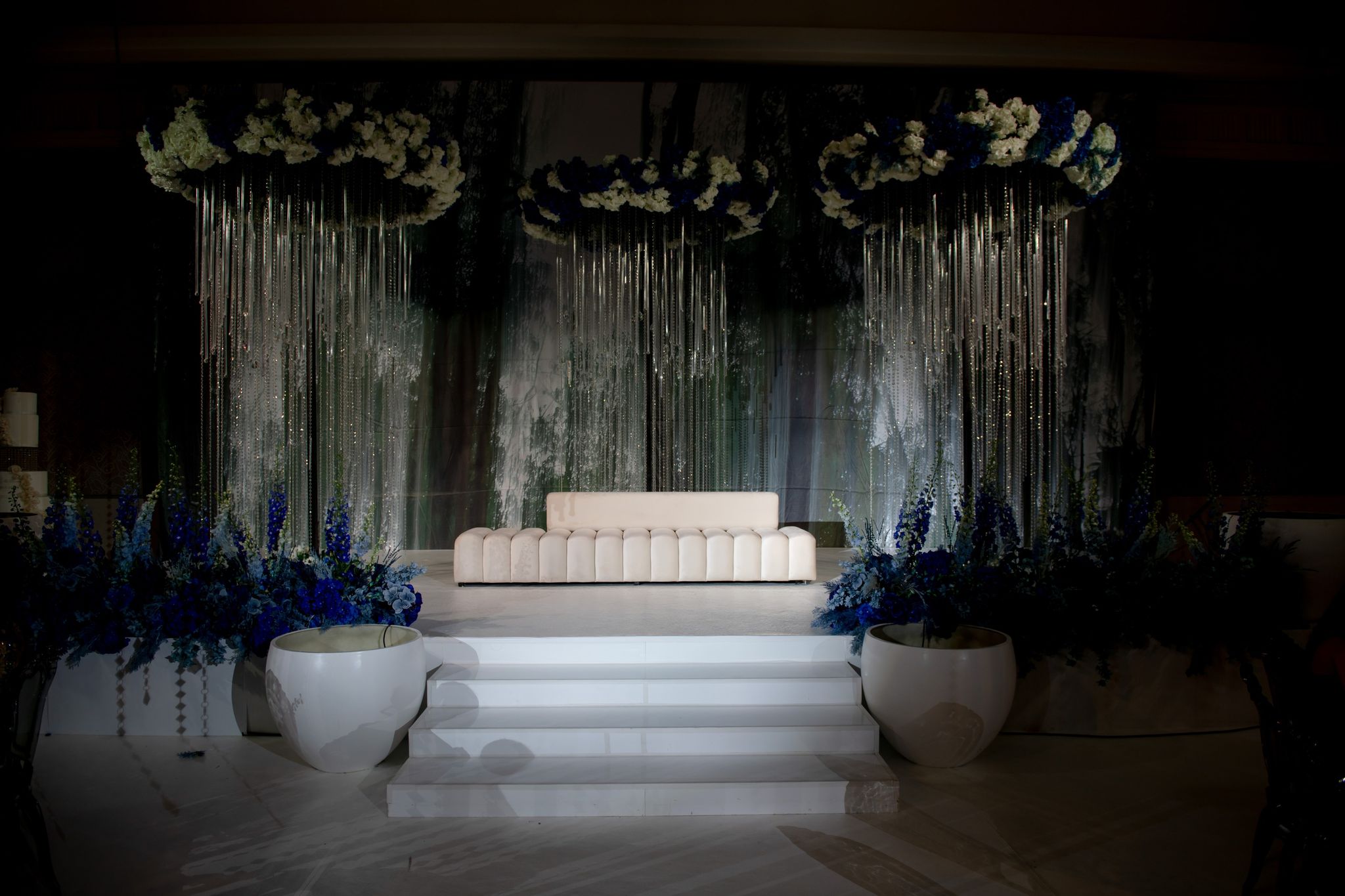 Stepped white stage with a channel-tufted sofa under three crystal-hung floral rings at Four Seasons Resort Dubai at Jumeirah Beach