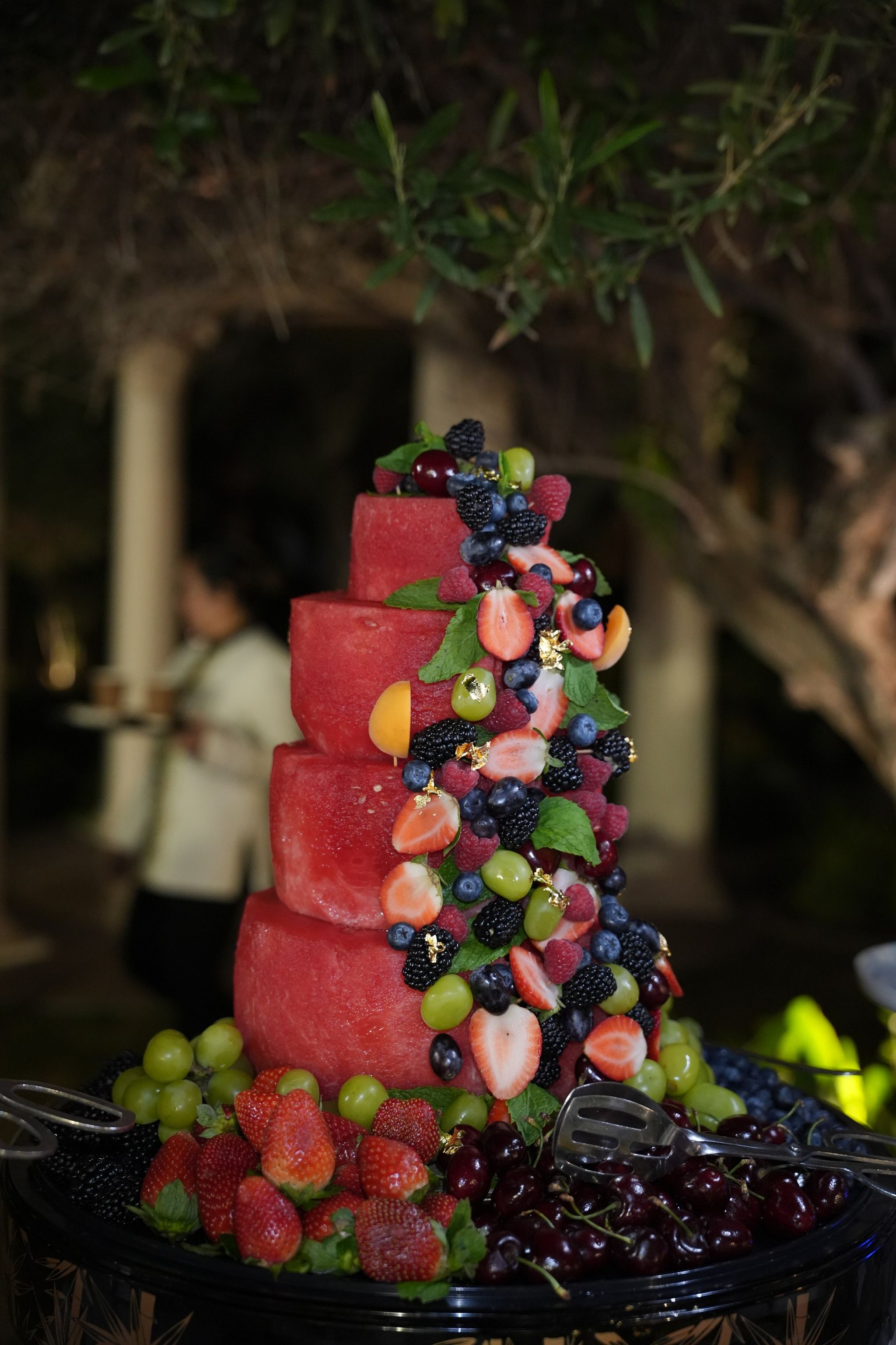 Tiered watermelon cake dressed with berries, grapes and strawberries on an evening buffet