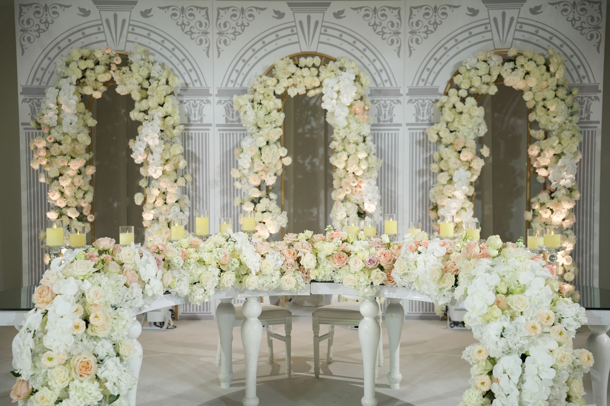 Frontal view of the head table, candles glowing beneath three arches of ivory and peach roses
