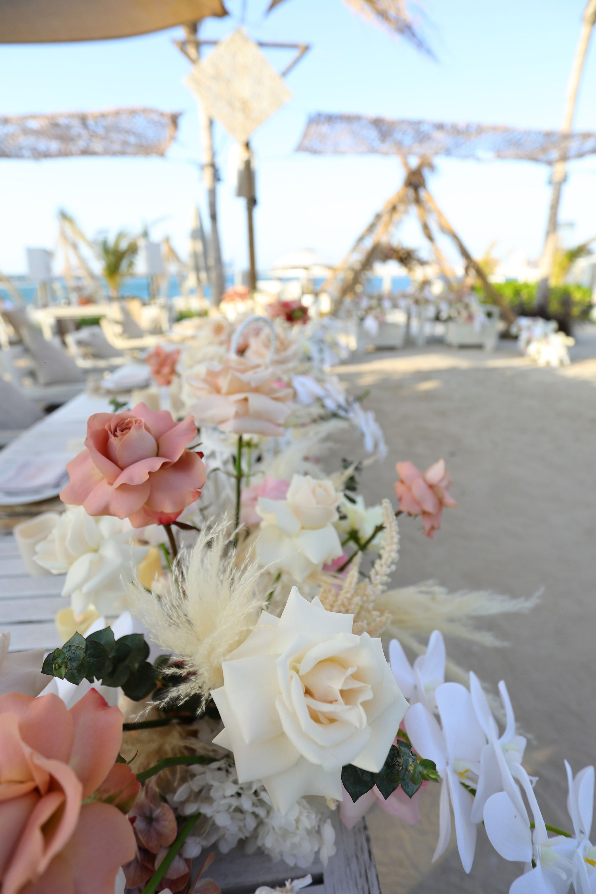 Long table runner of roses, orchids and pampas leading towards woven canopies at Jumeirah Zabeel Saray