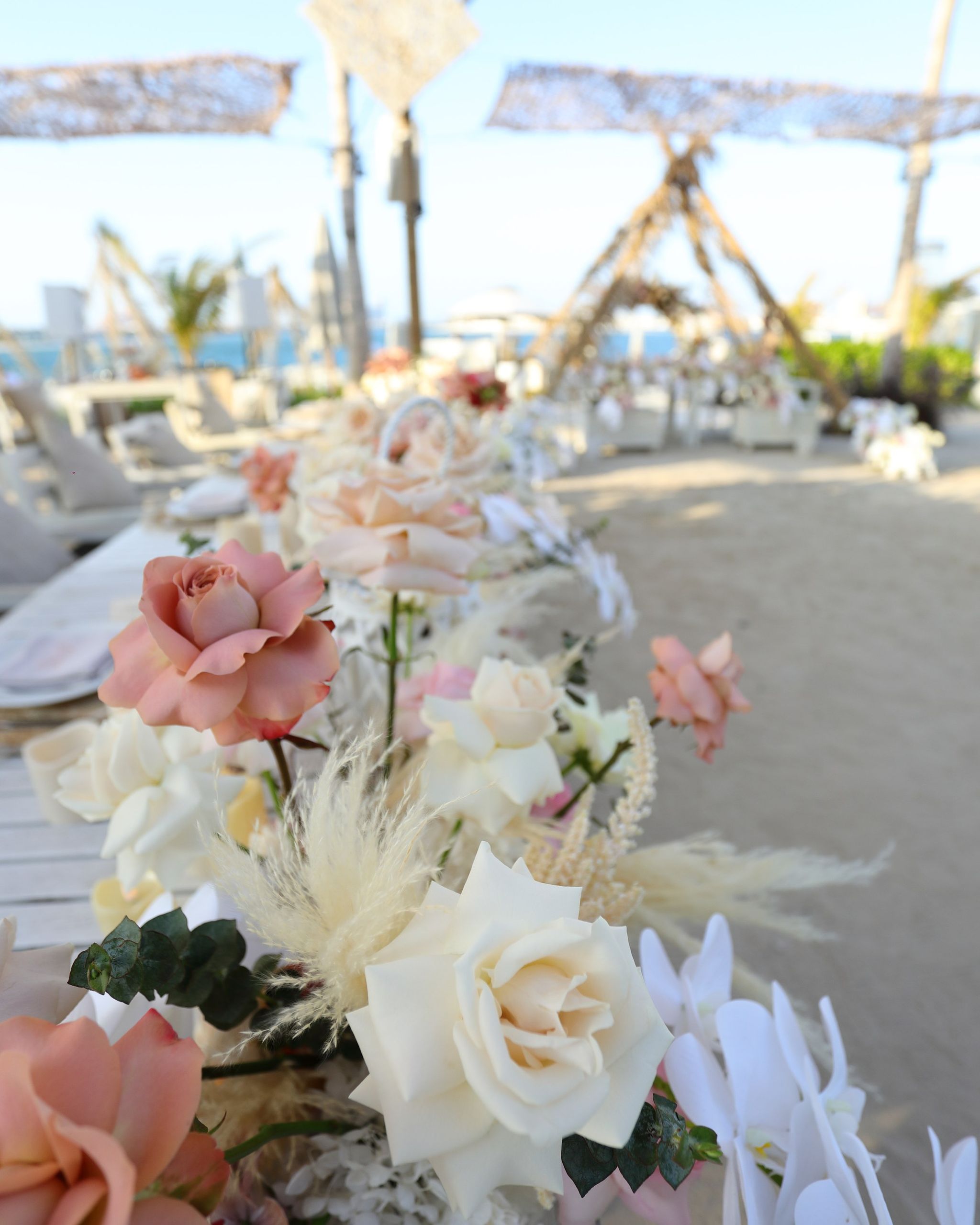 Long table runner of roses, orchids and pampas leading towards woven canopies at Jumeirah Zabeel Saray