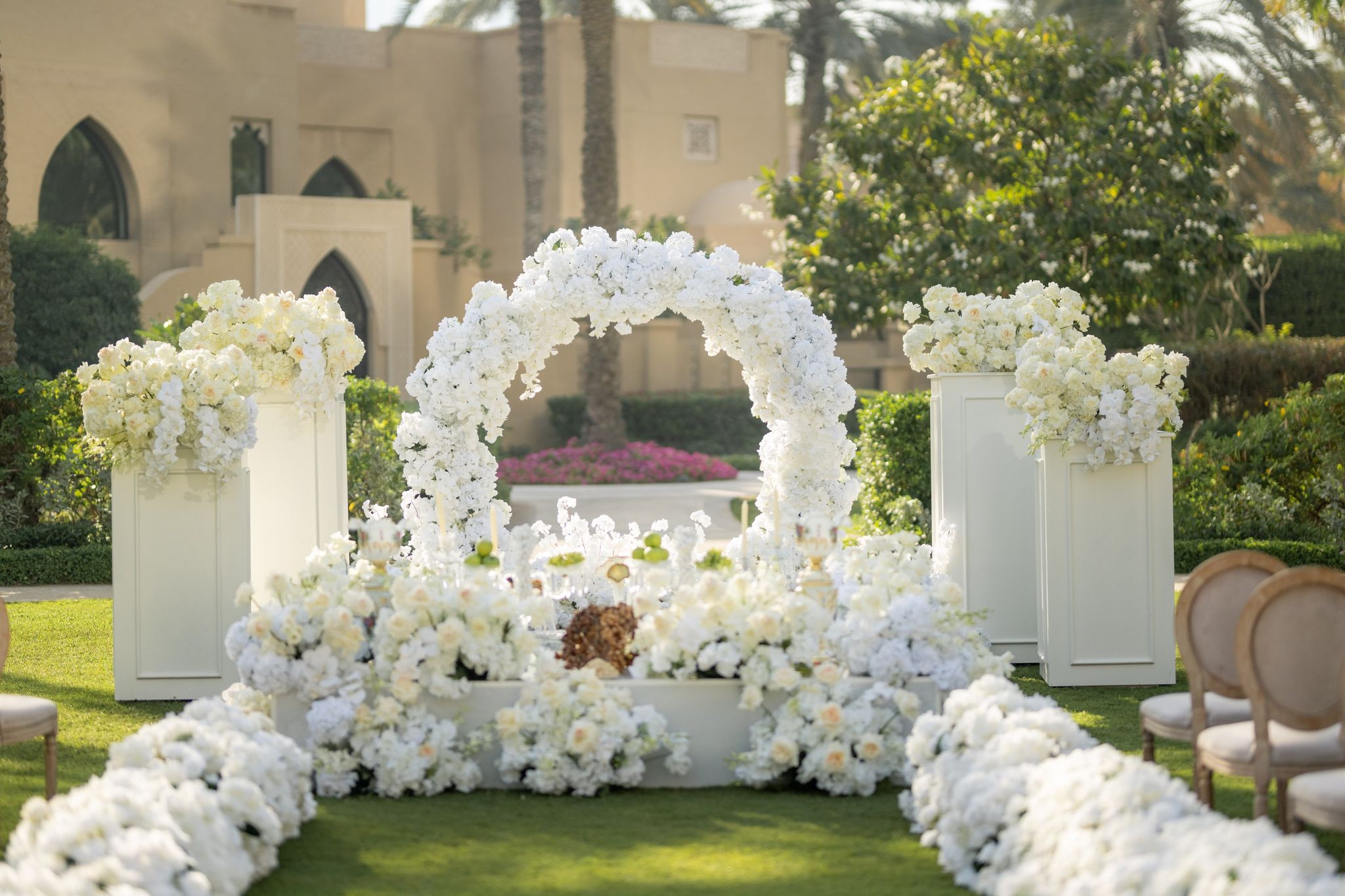Round arch of white blooms over the sofreh, flanked by white plinths of roses