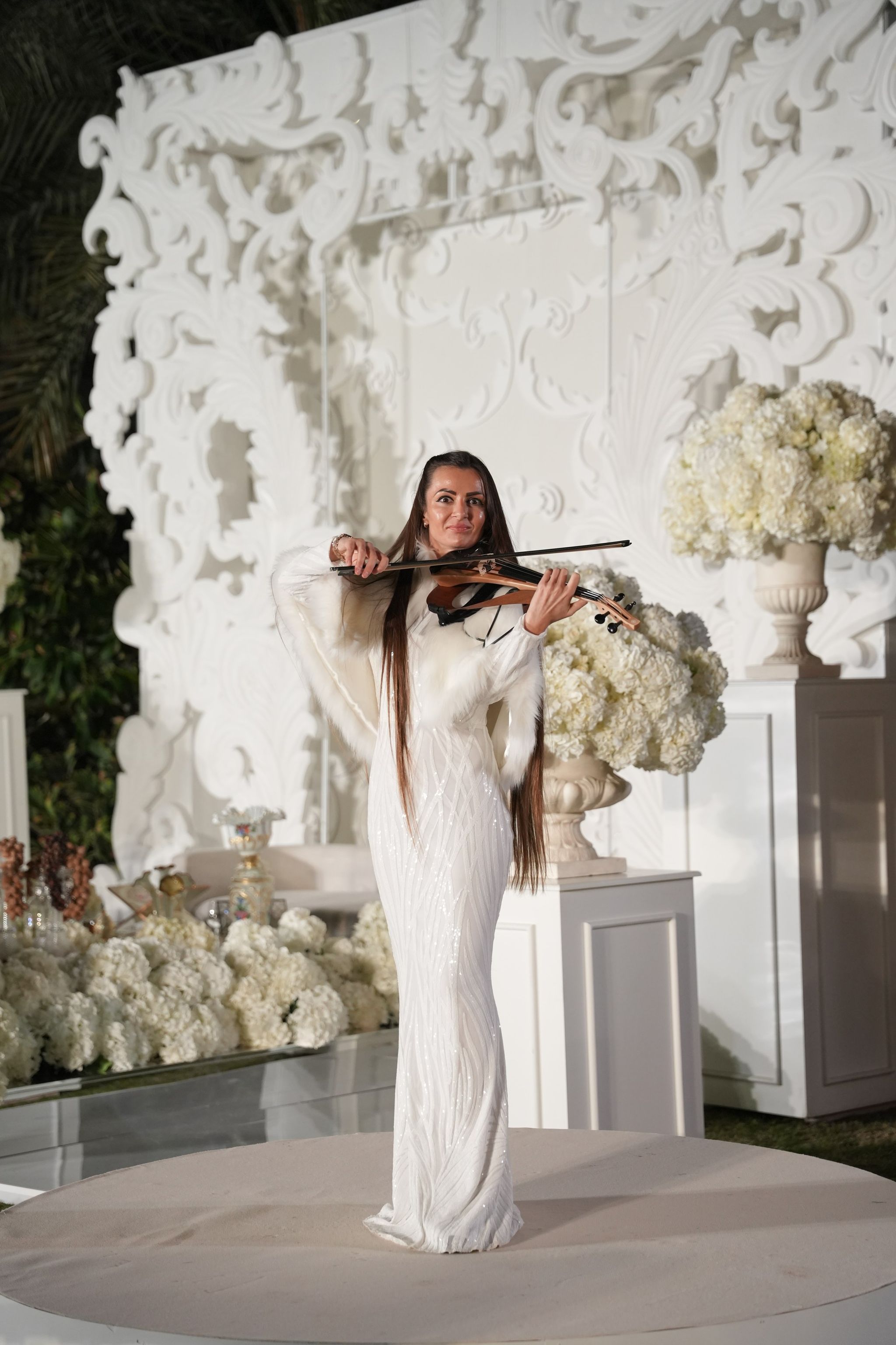 A violinist in a white sequinned gown performing before the carved backdrop at Raffles The Palm Dubai