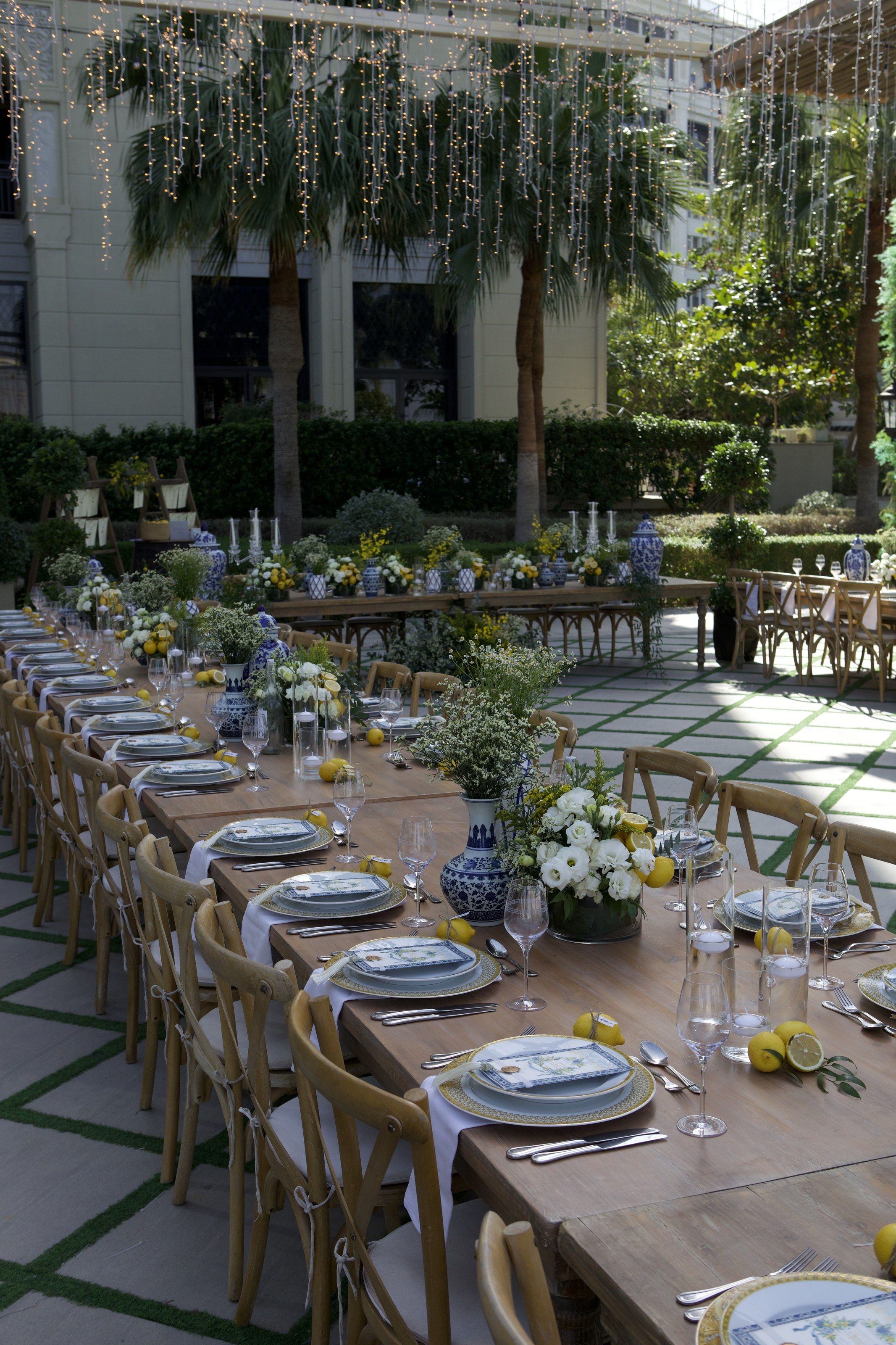 Long tables beneath strands of hanging lights and palms, set with lemons and white flowers