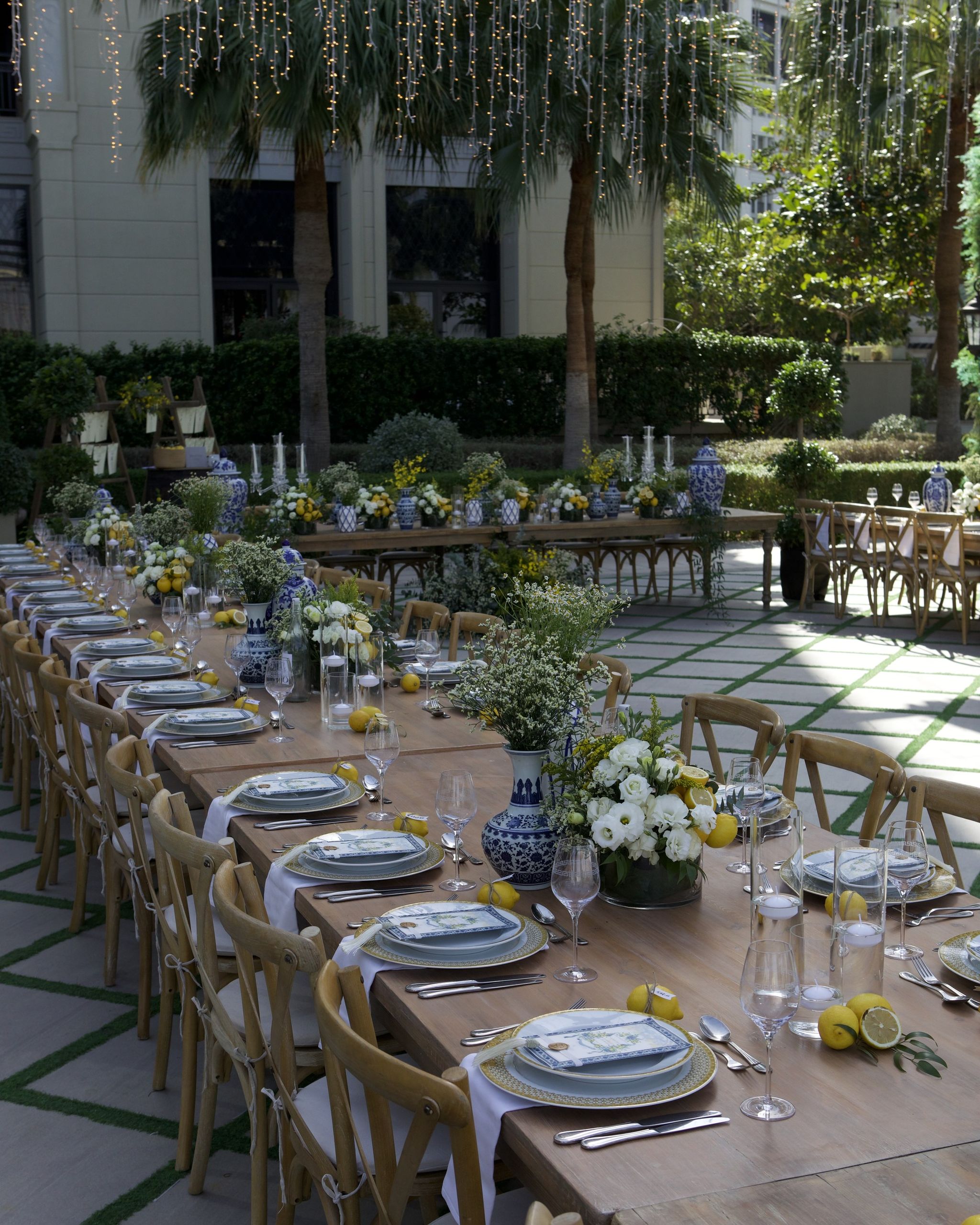 Long tables beneath strands of hanging lights and palms, set with lemons and white flowers