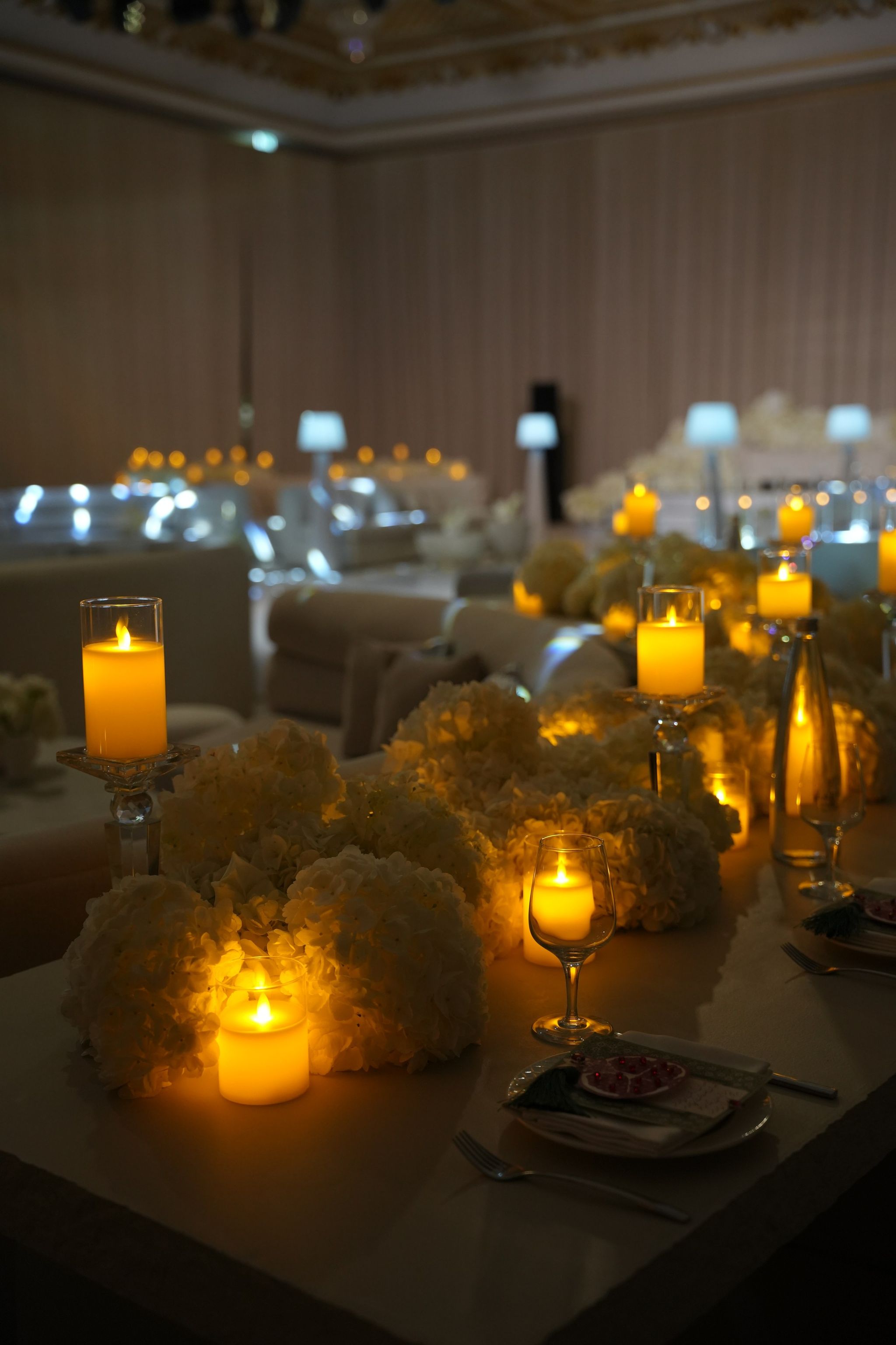 Long table lined with white hydrangeas and glowing pillar candles in the ballroom