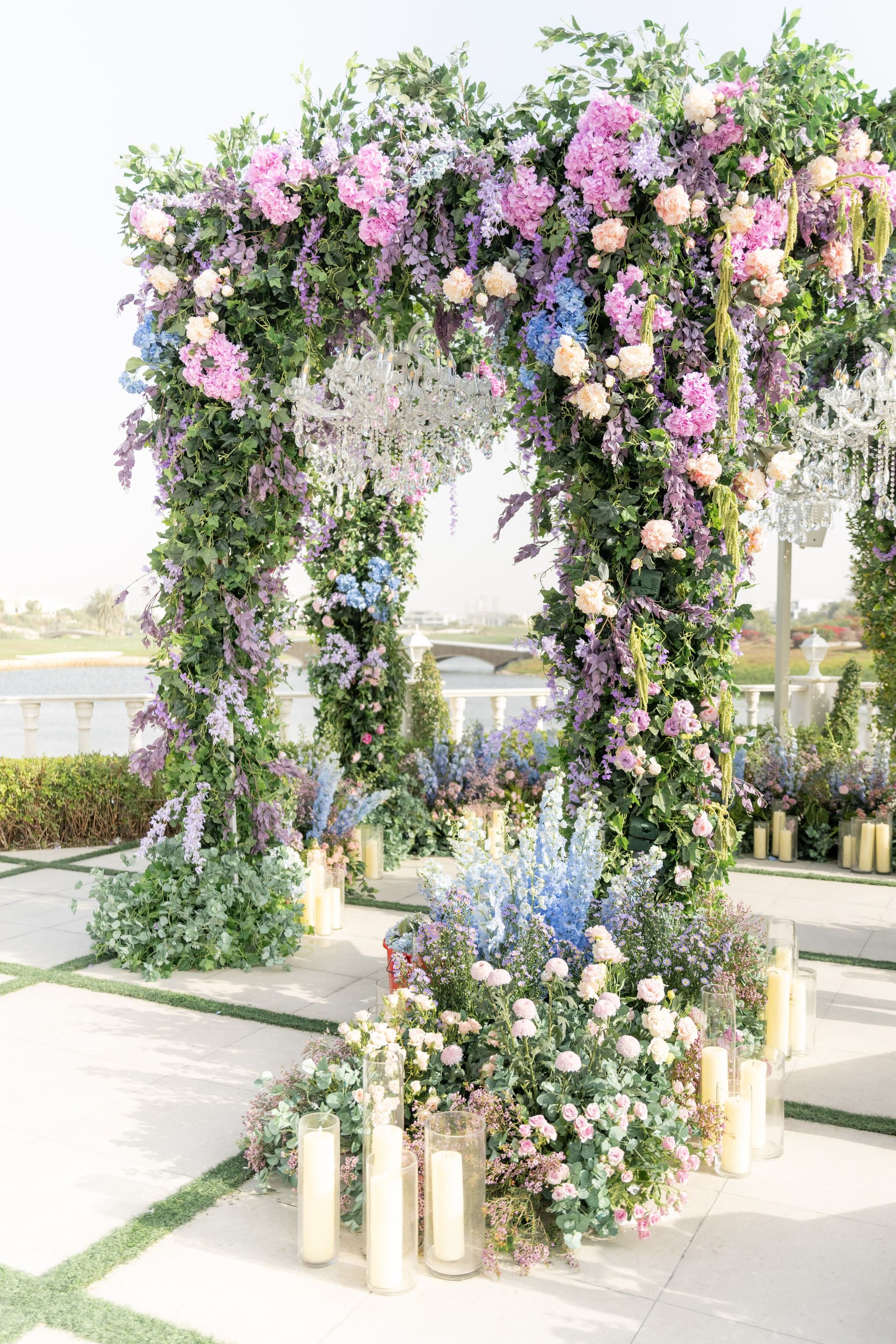 Corner of the floral canopy with delphinium, roses and pillar candles beside a lakeside balustrade