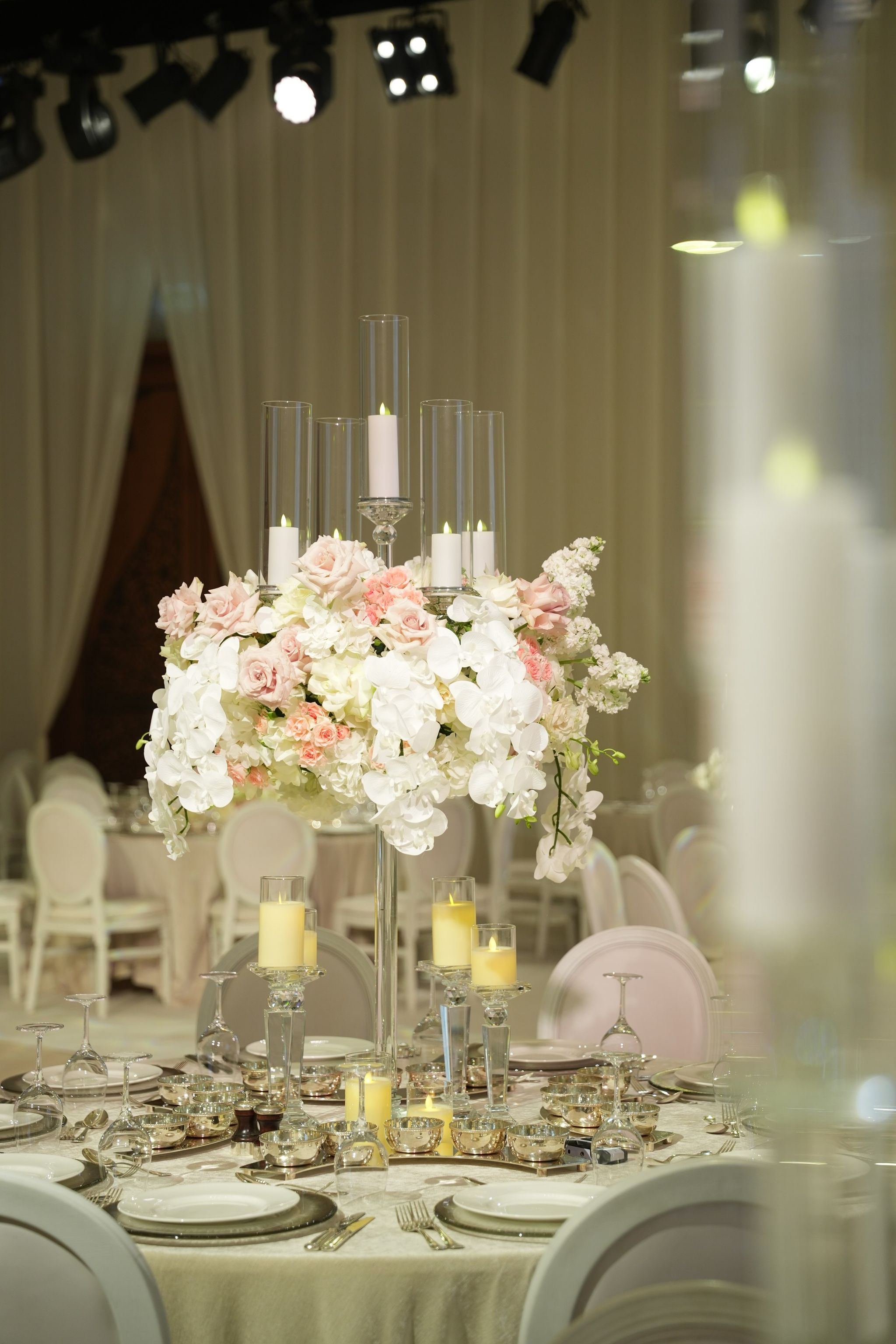 Crystal candelabra crowned with white orchids and blush roses above an ivory-linen table