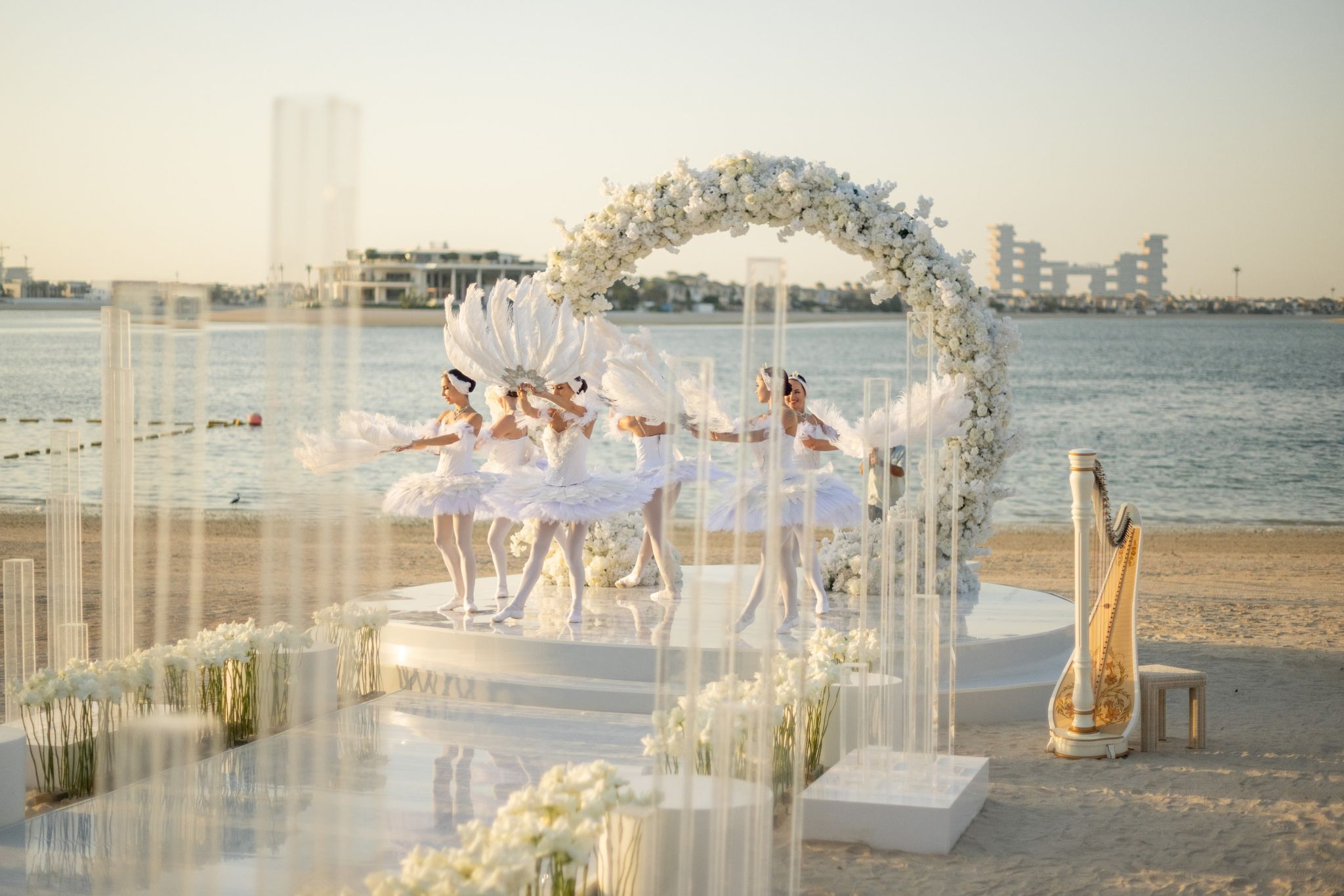 Ballerinas in white tutus dancing on the round stage, a gilded harp and acrylic columns beside them