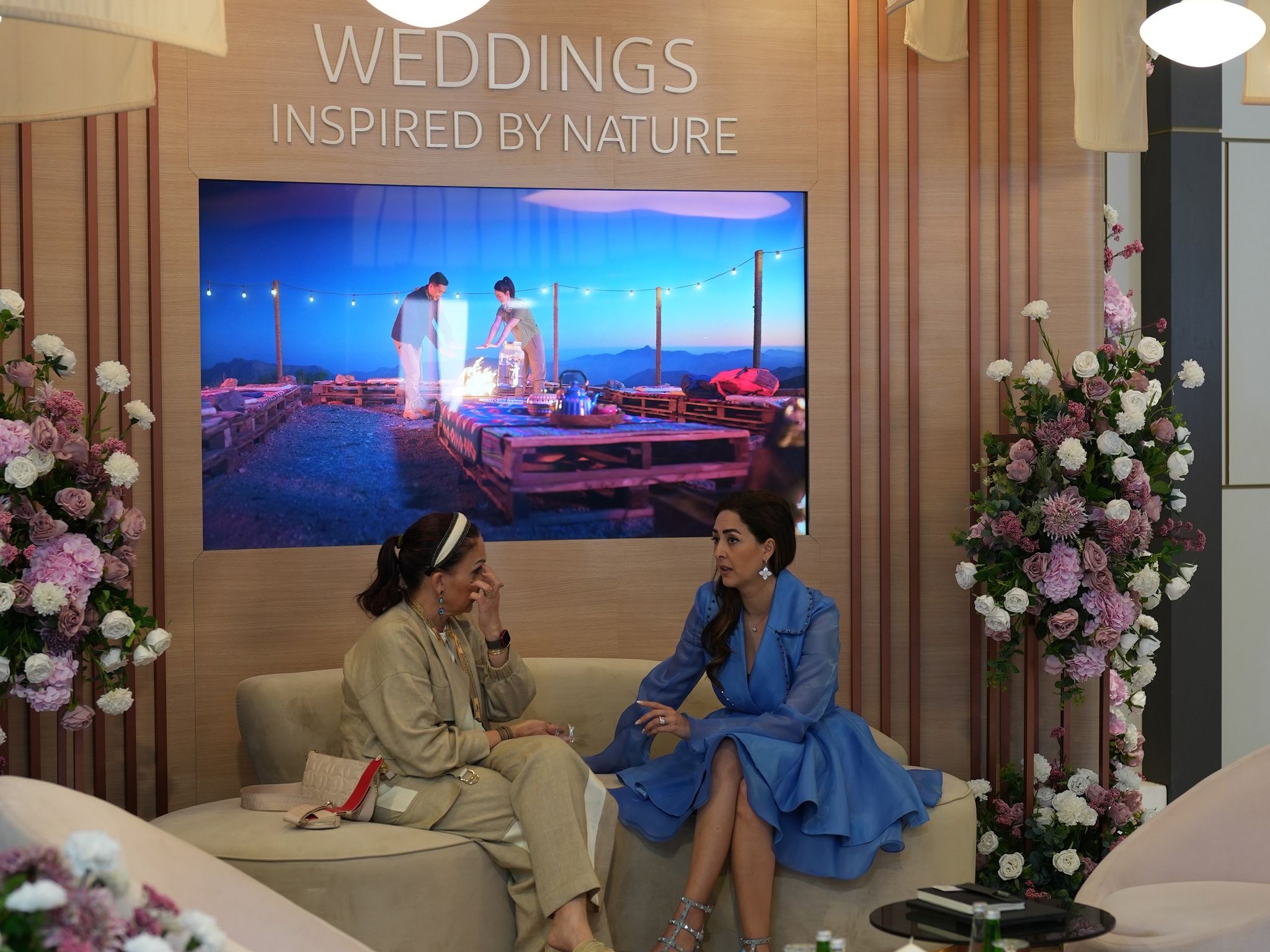 Exhibition lounge with curved blush seating, hydrangea columns and fabric canopies beneath a wedding screen