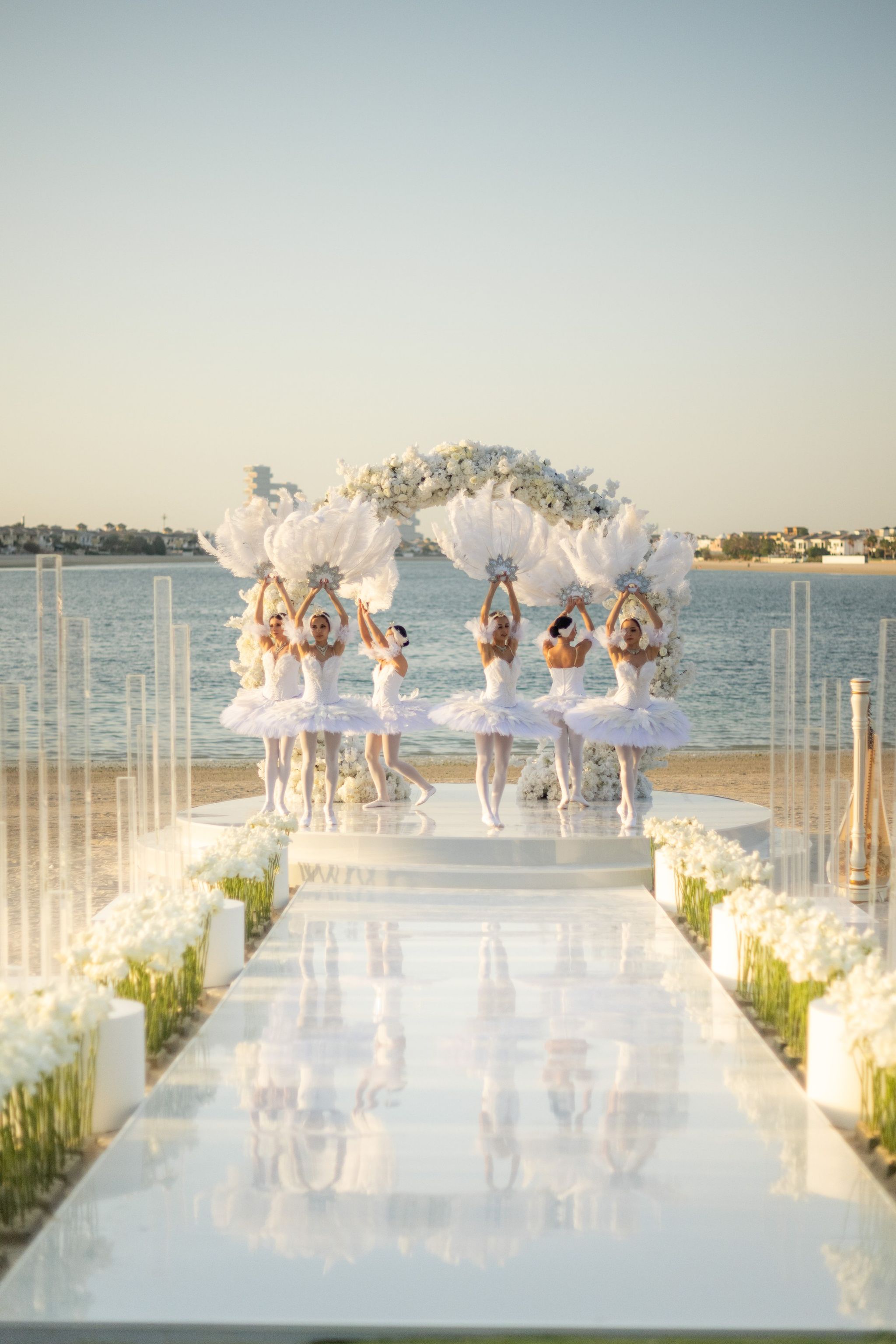 Ballerinas raising feather fans beneath the floral arch, reflected in a mirrored aisle