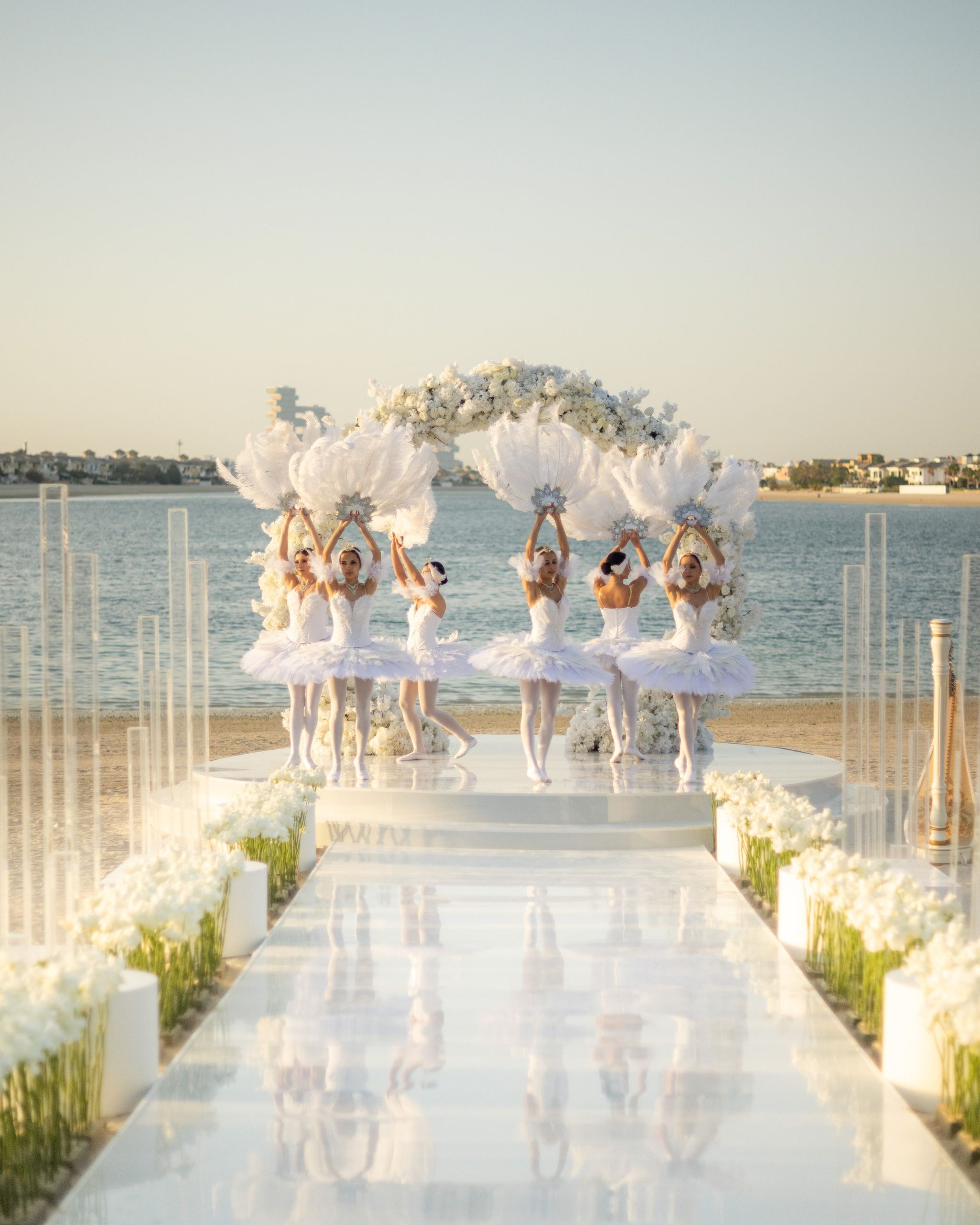 Ballerinas raising feather fans beneath the floral arch, reflected in a mirrored aisle