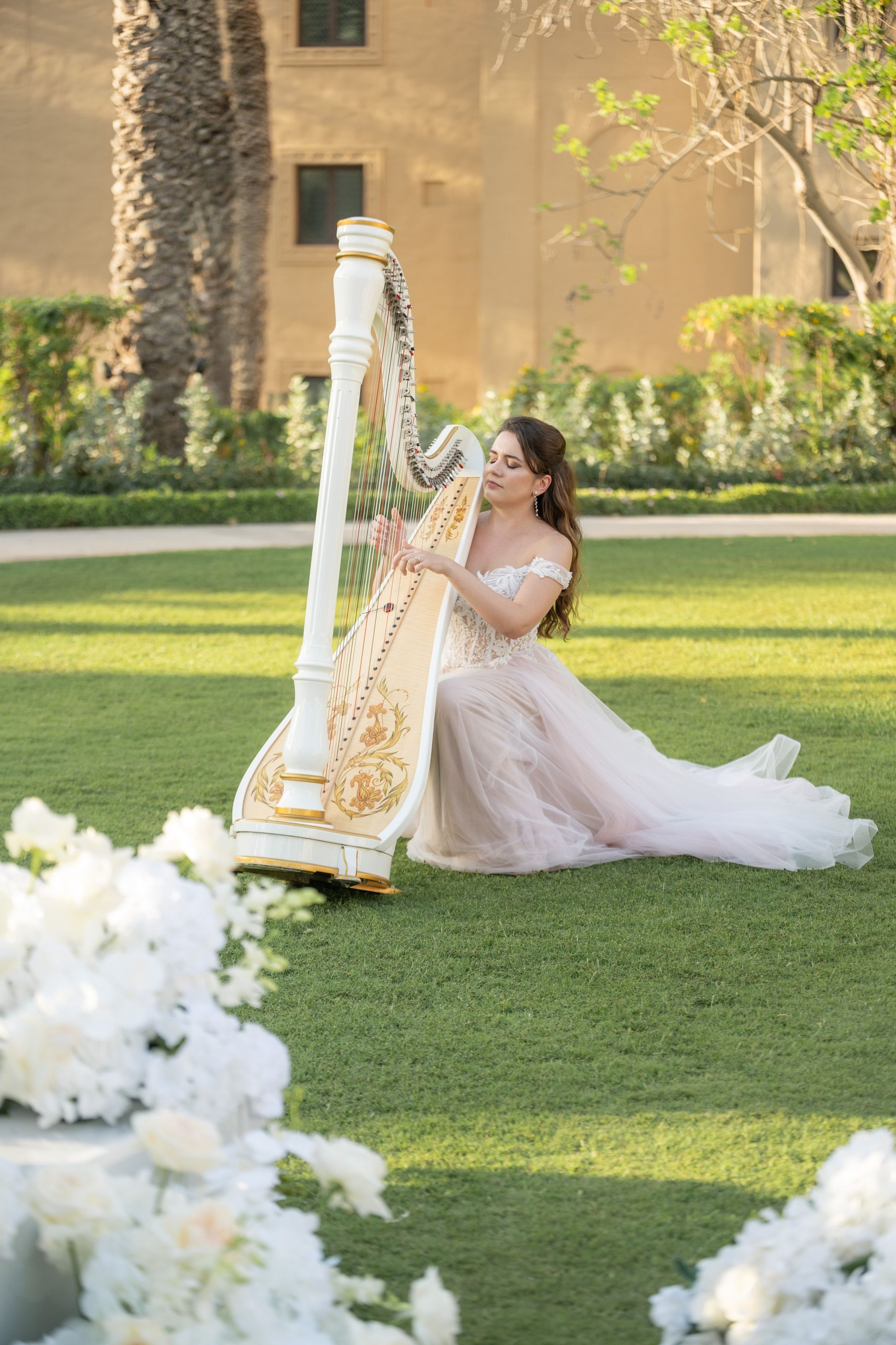Harpist in a blush tulle gown playing a white and gold harp on the lawn