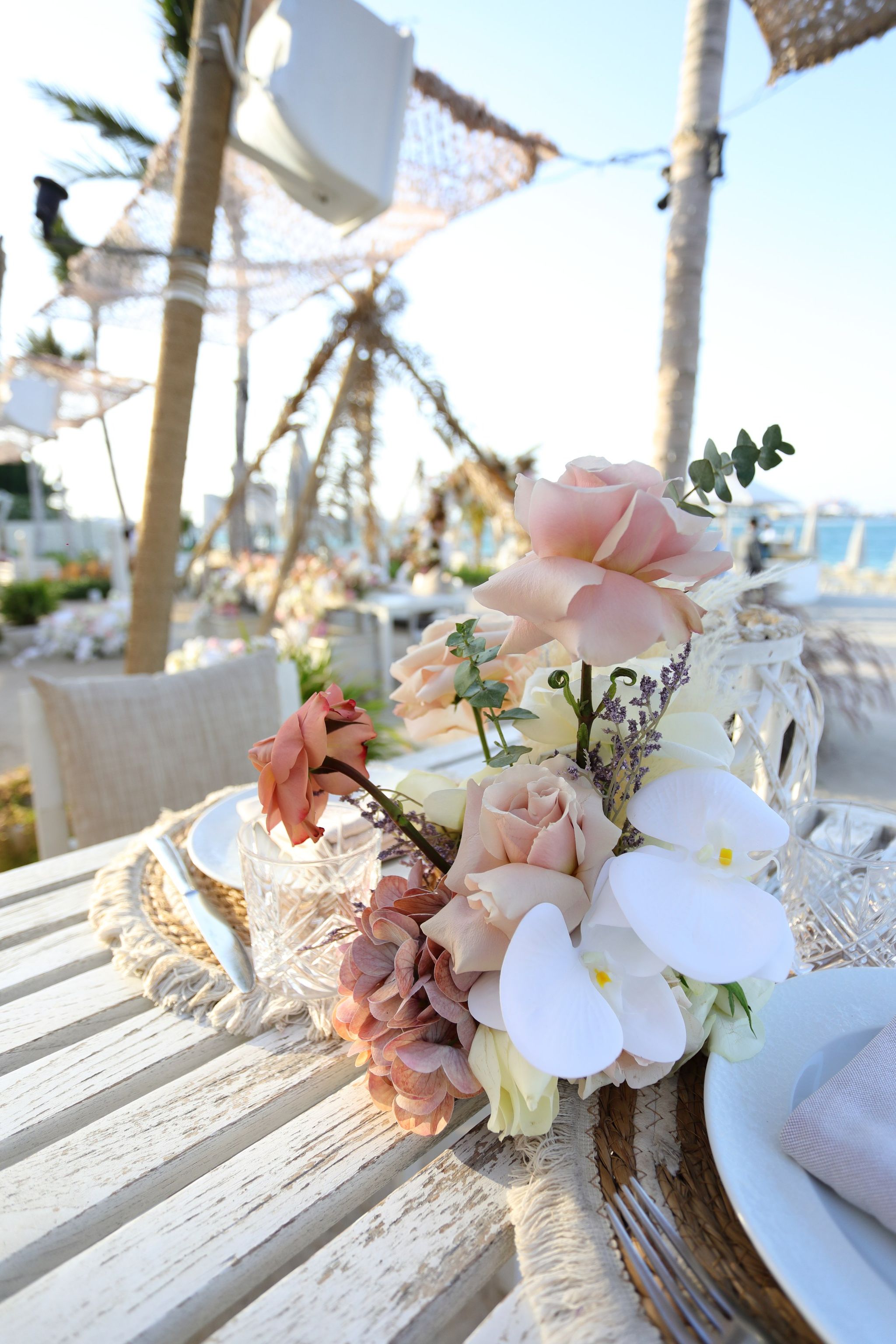 Posy of blush roses and white orchids beside cut-crystal glassware on a whitewashed table