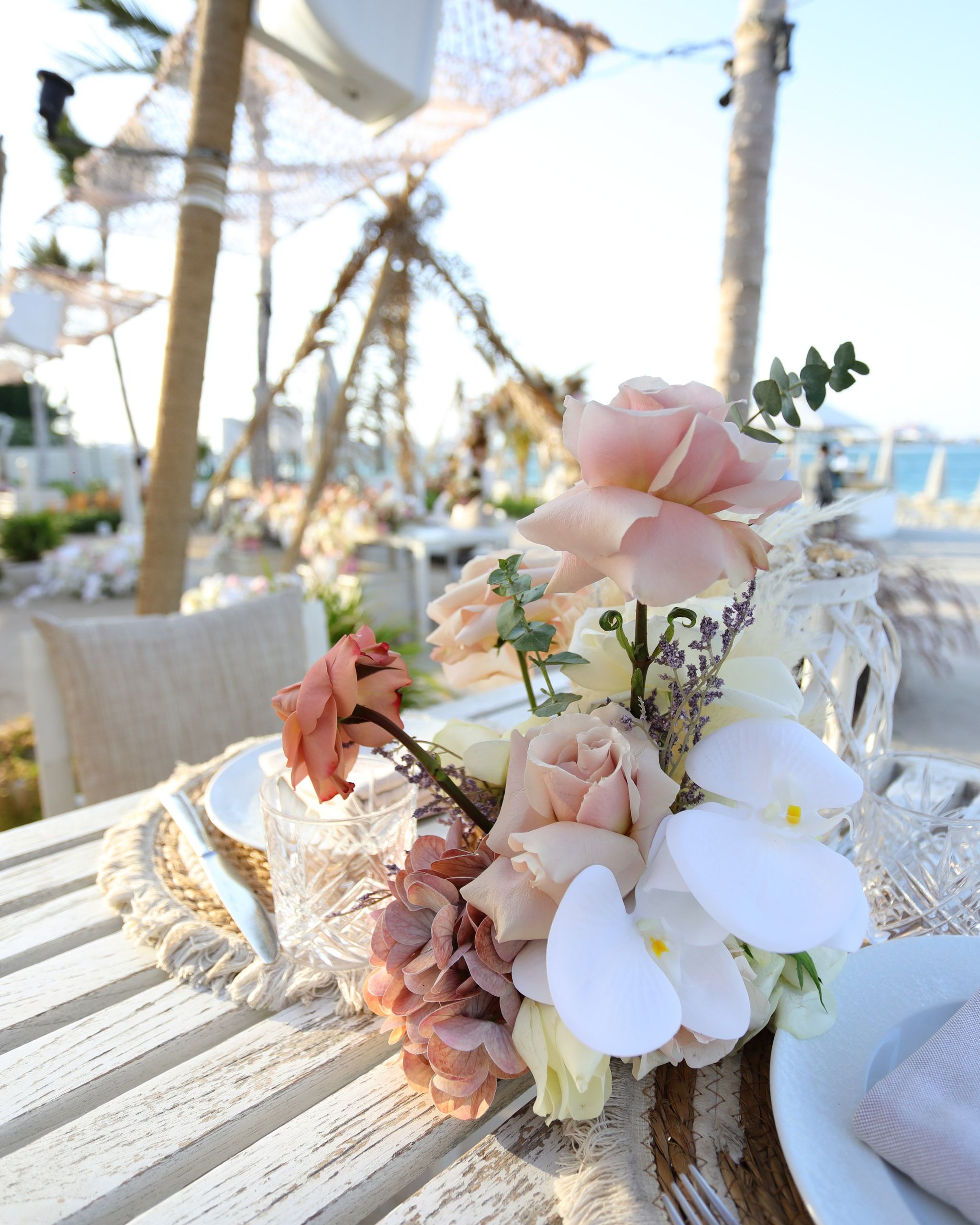 Posy of blush roses and white orchids beside cut-crystal glassware on a whitewashed table
