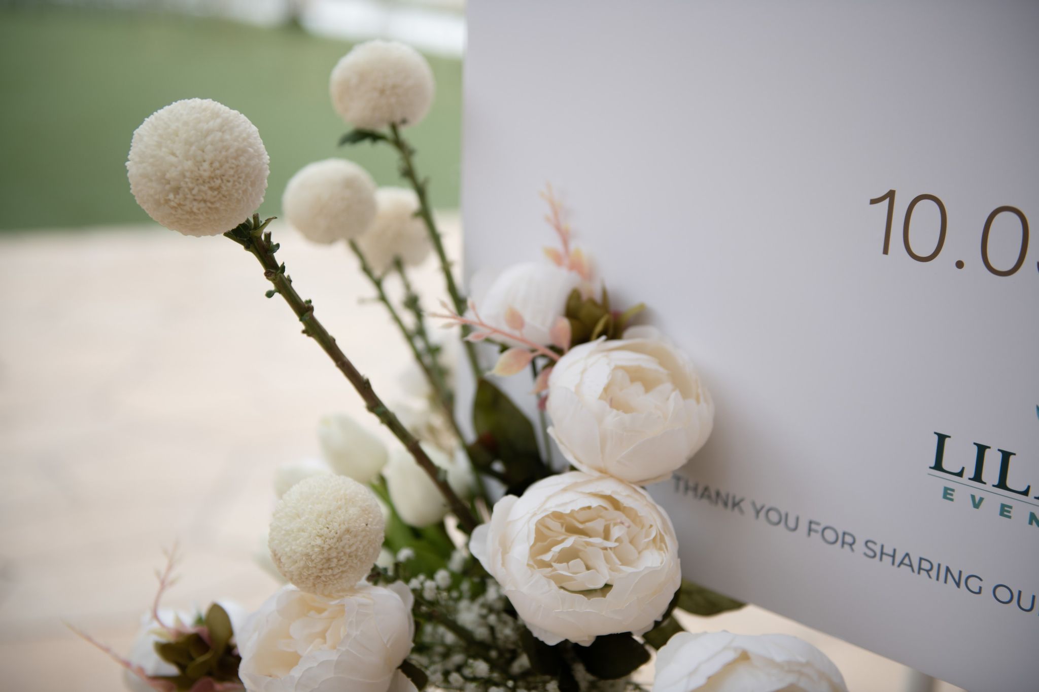 Ivory peonies and white ball blooms beside a thank-you welcome sign