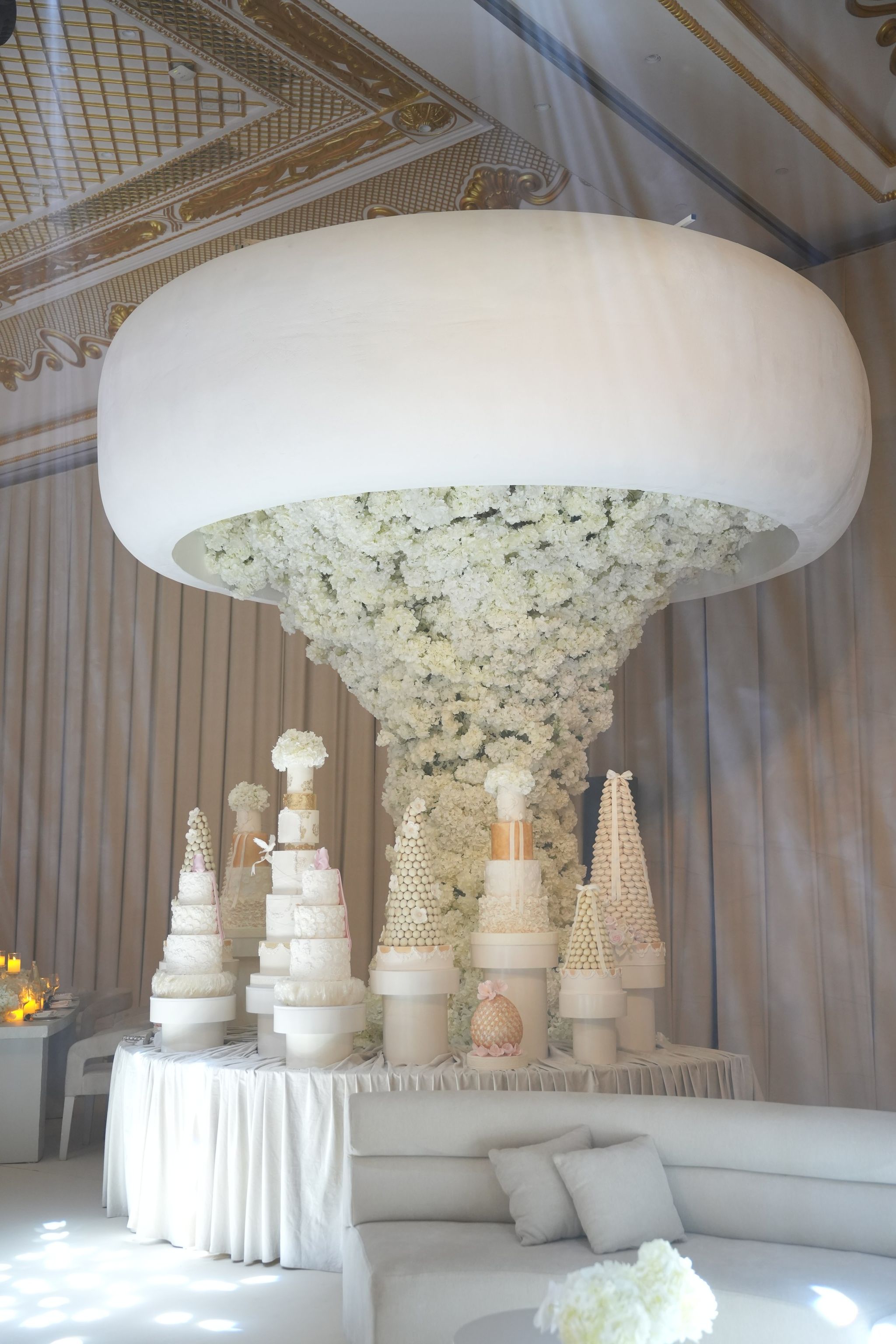 Suspended white disc trailing a cascade of white flowers over a table of tiered wedding cakes
