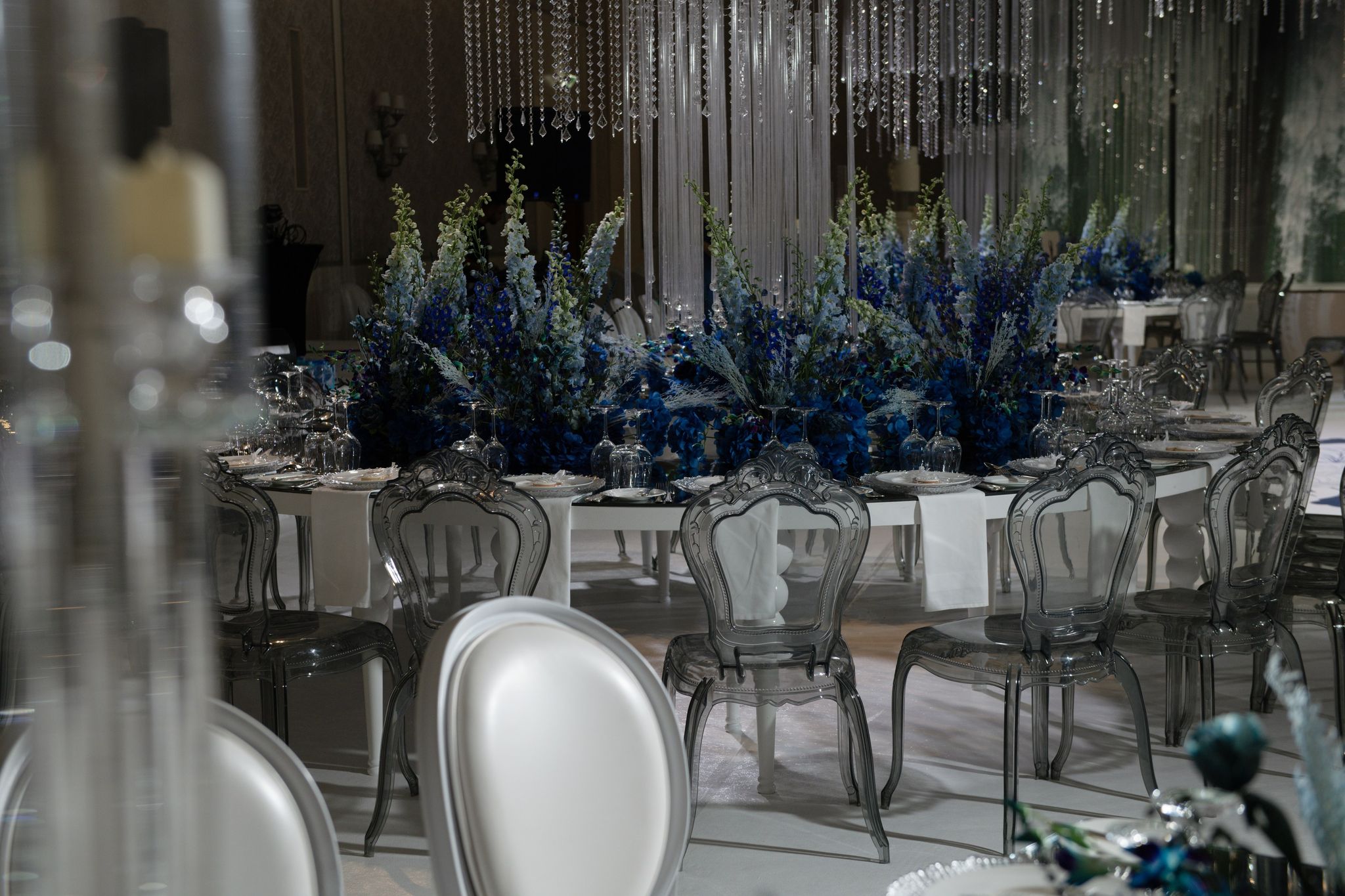 Long table of cobalt delphiniums and hydrangeas with clear carved chairs at Four Seasons Resort Dubai at Jumeirah Beach