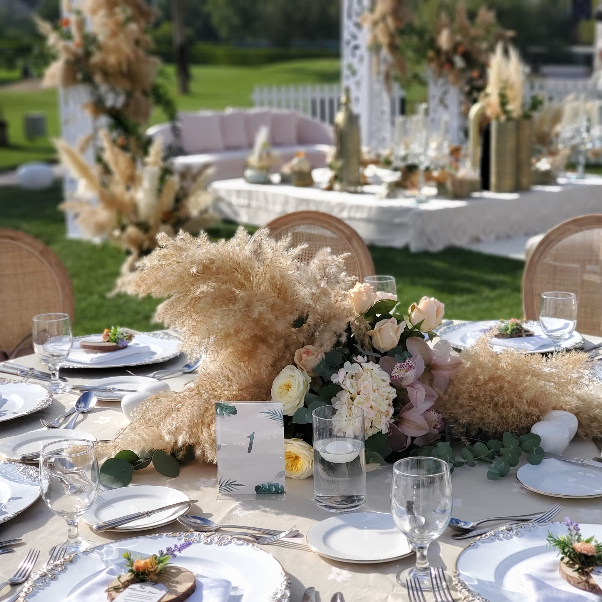 Pampas and garden rose centrepiece with table number and floating candle, ceremony lounge softly behind