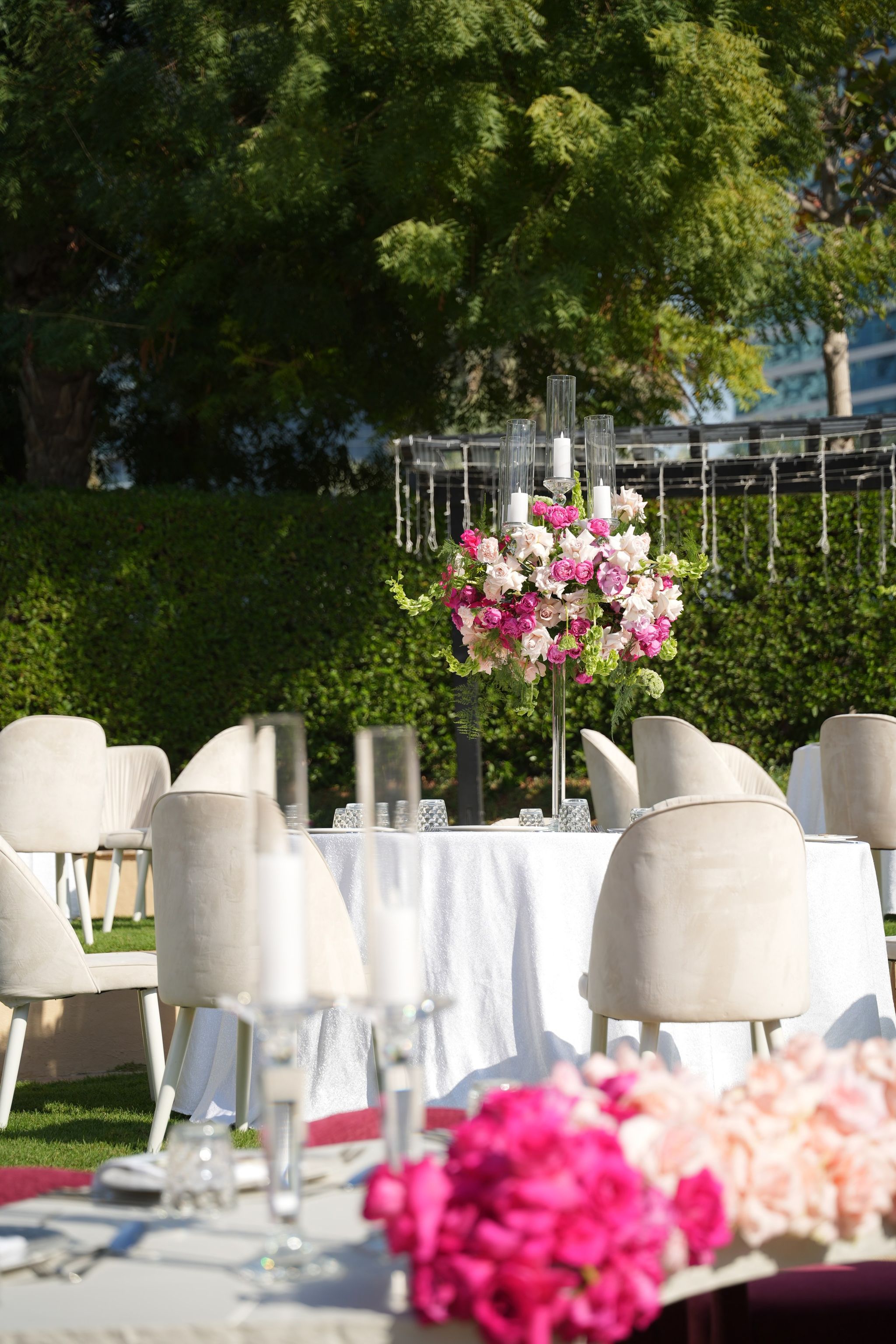 Raised candelabra of pink roses over a white-clothed table with ivory velvet chairs