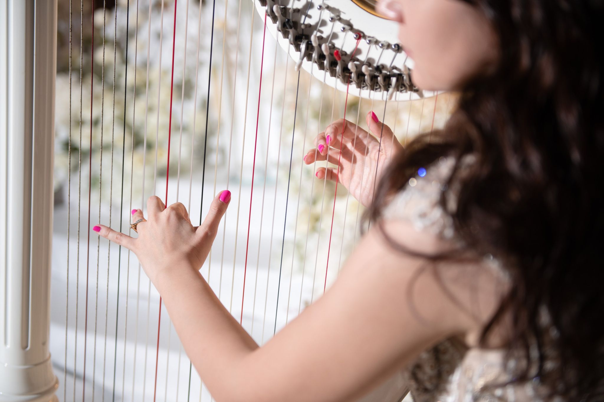 Close view of a harpist's hands on the strings, with white florals softly blurred behind