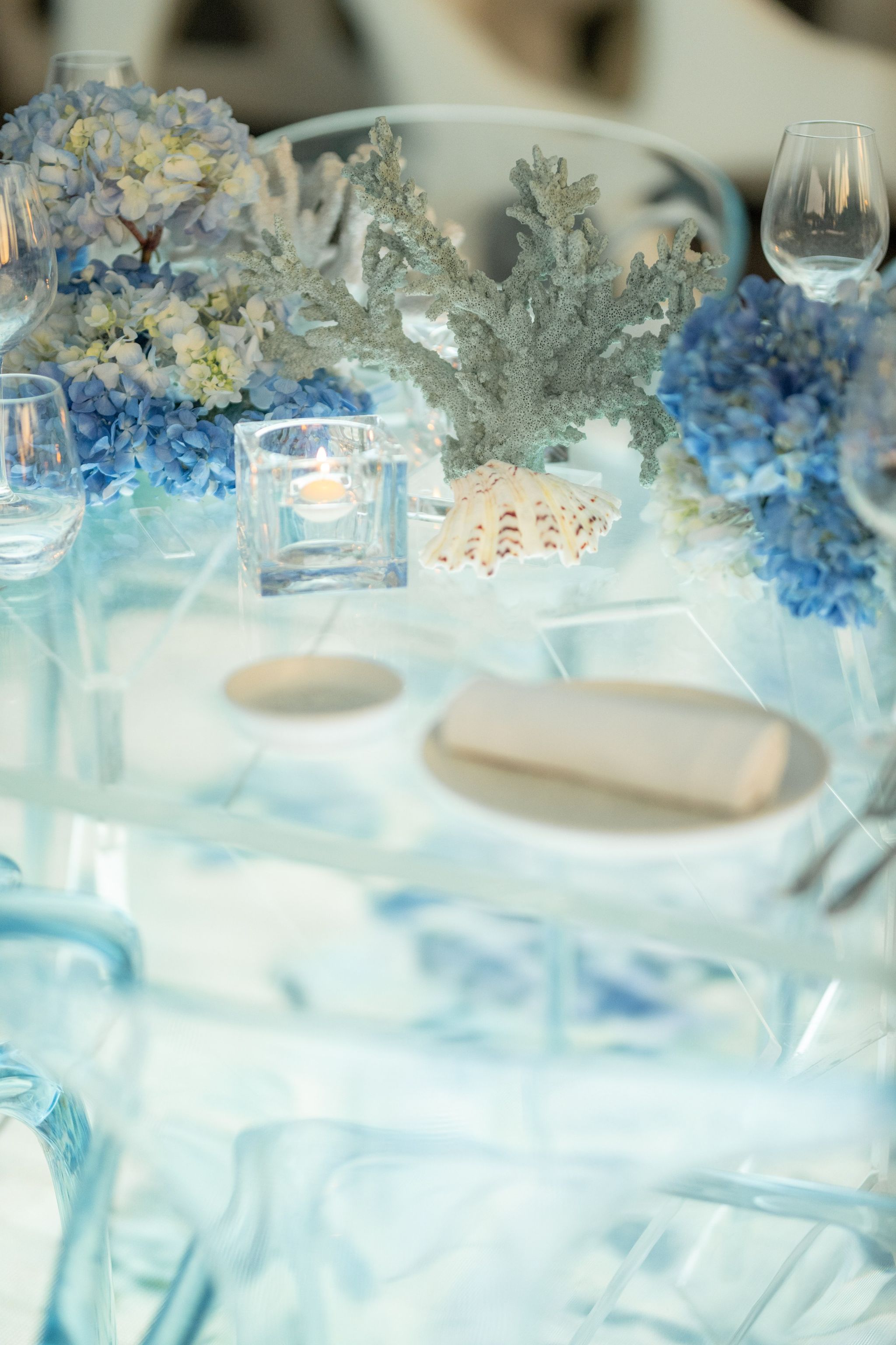 Coral and scallop shell centrepiece beside a linen napkin and votive on the acrylic table