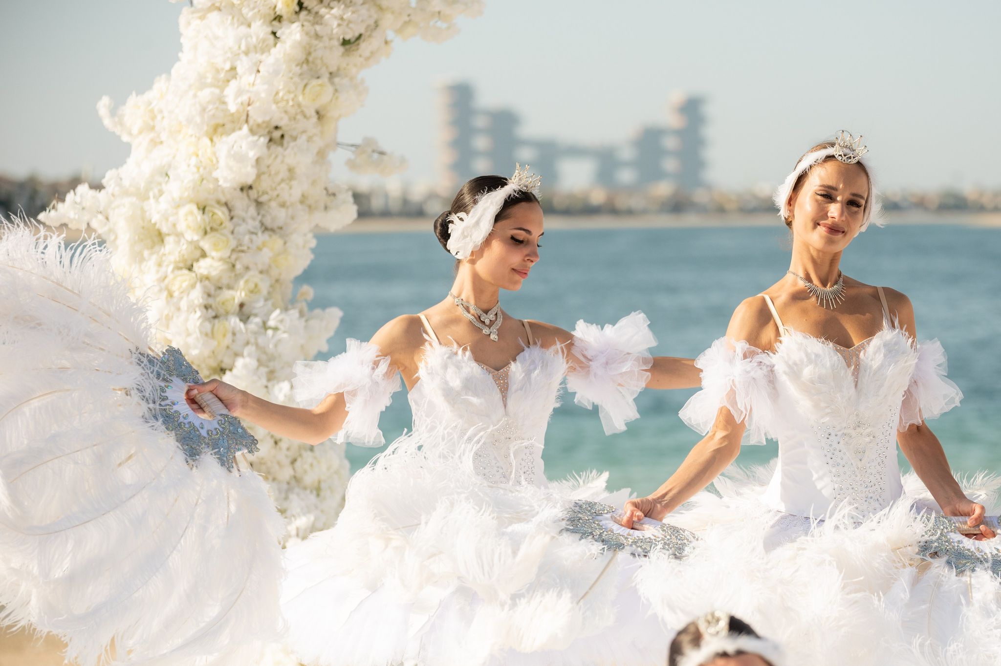 Two ballerinas in feathered white costumes and tiaras performing by the arch on Palm Jumeirah