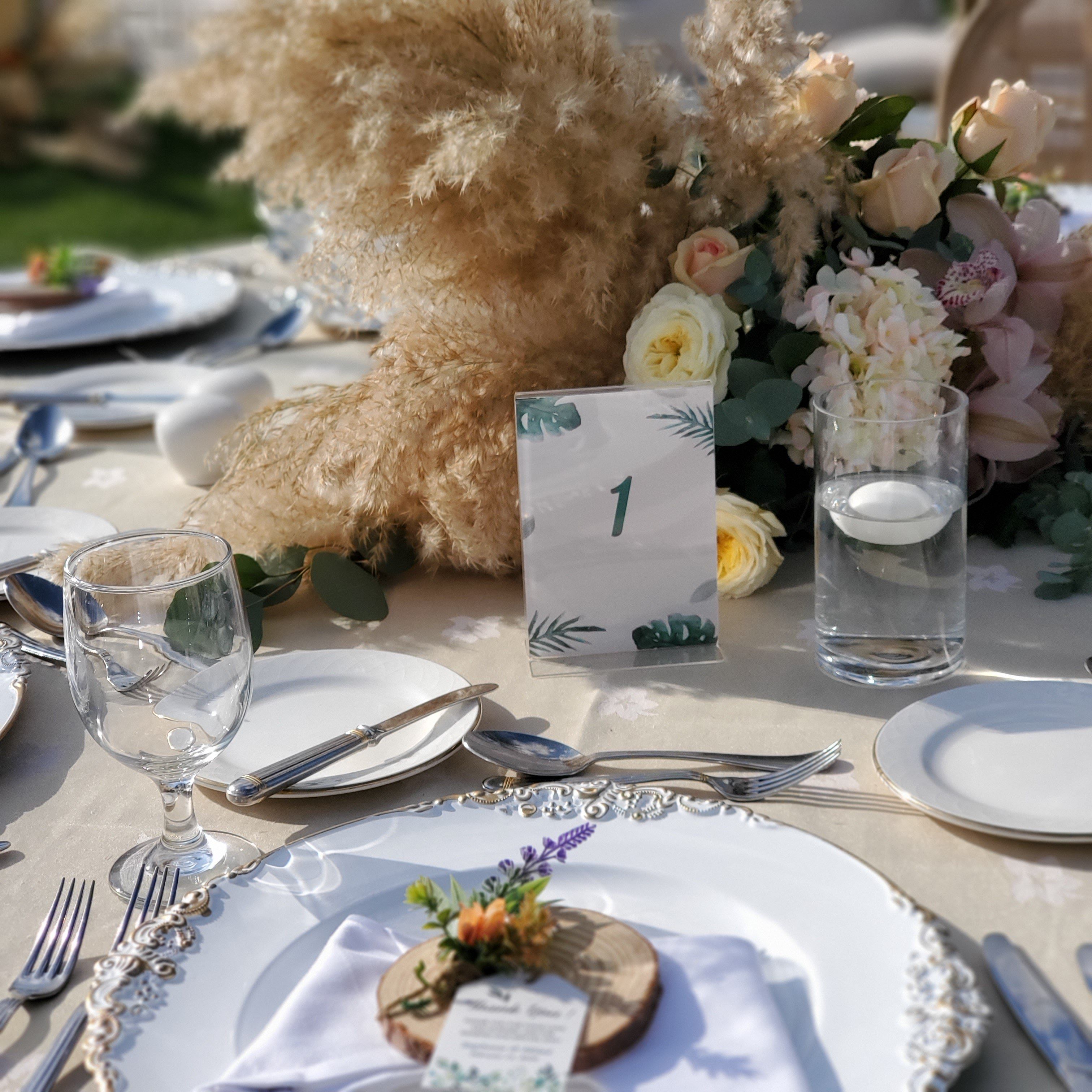 Gold-rimmed place setting with a wood-slice name tag and sprig of lavender beside pampas grass