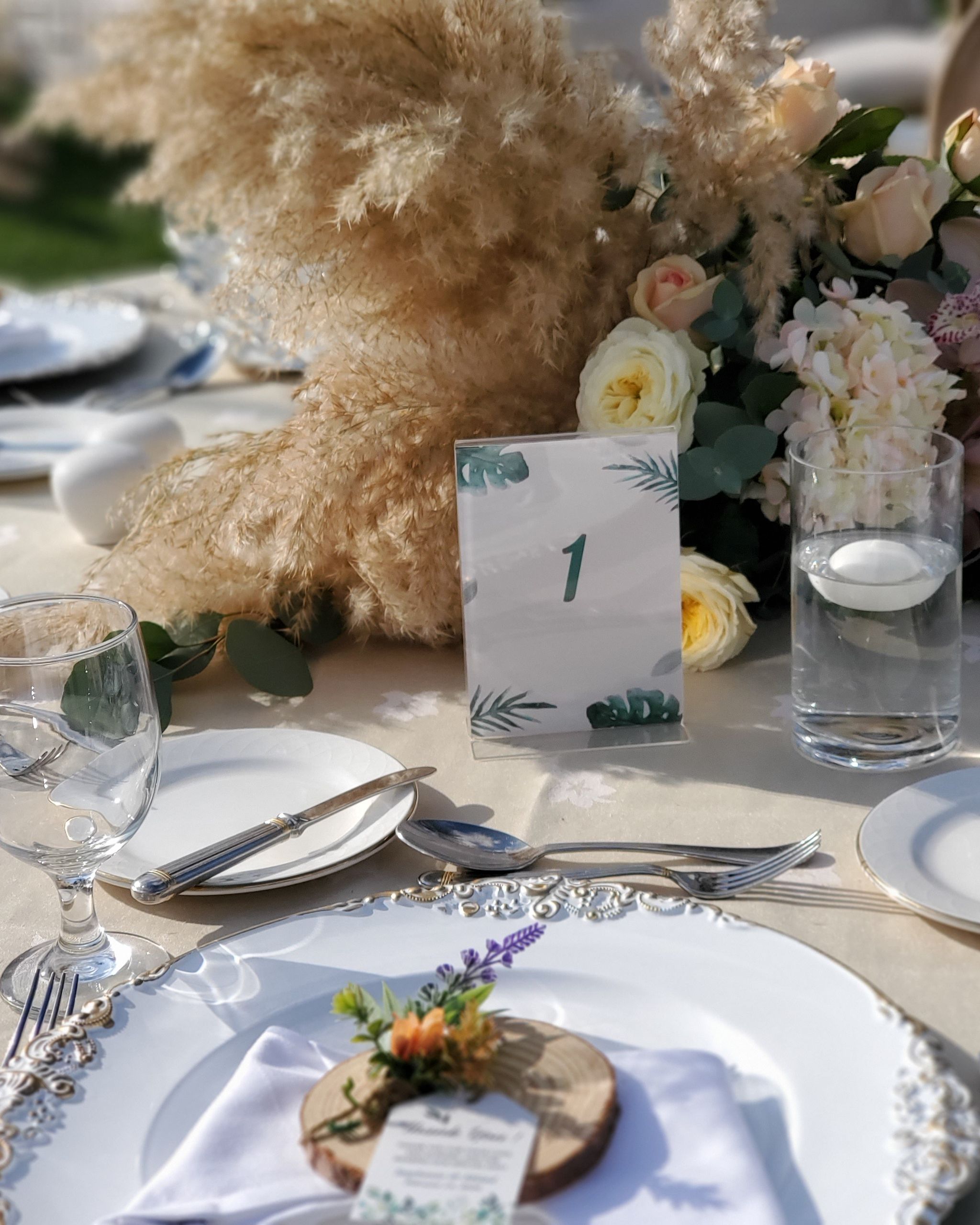 Gold-rimmed place setting with a wood-slice name tag and sprig of lavender beside pampas grass