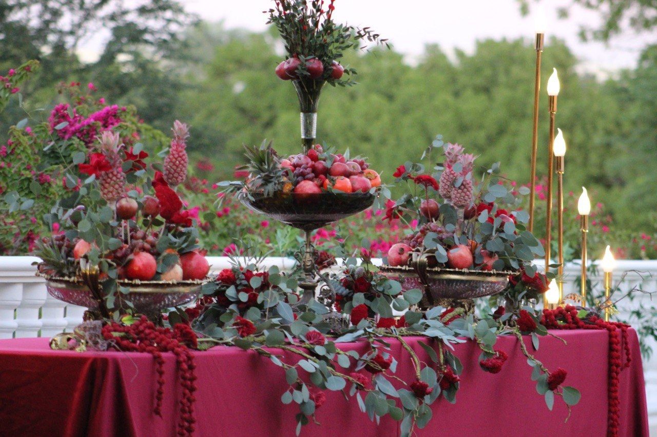 Yalda display of pomegranates, pineapples and fruit bowls on burgundy cloth with brass taper lamps