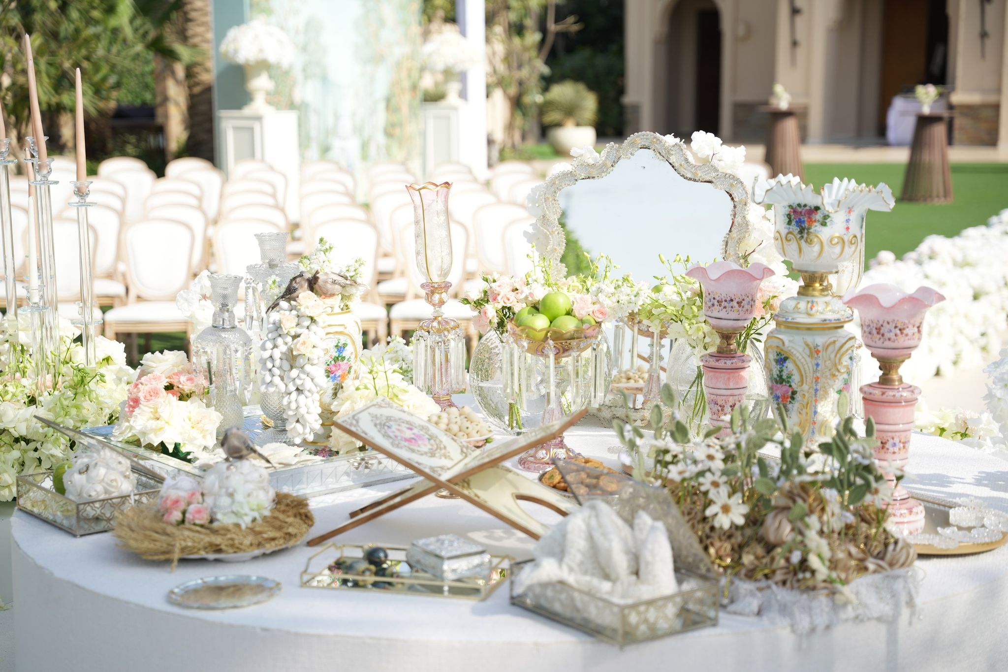 Sofreh aghd spread with an ornate mirror, open Quran stand, pink opaline vases and green apples