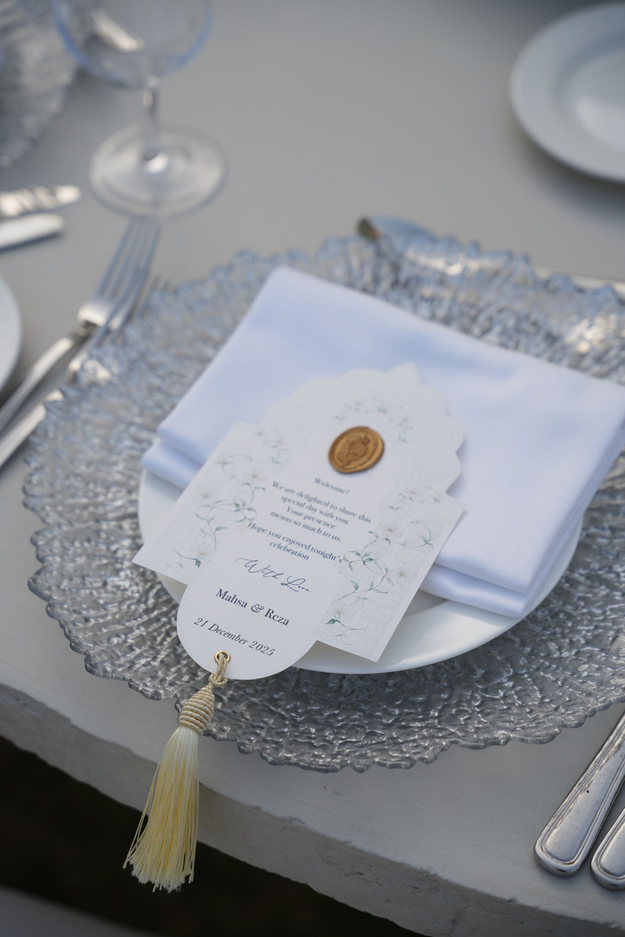 Arched welcome card with a gold wax seal and tassel on a folded napkin and silver charger