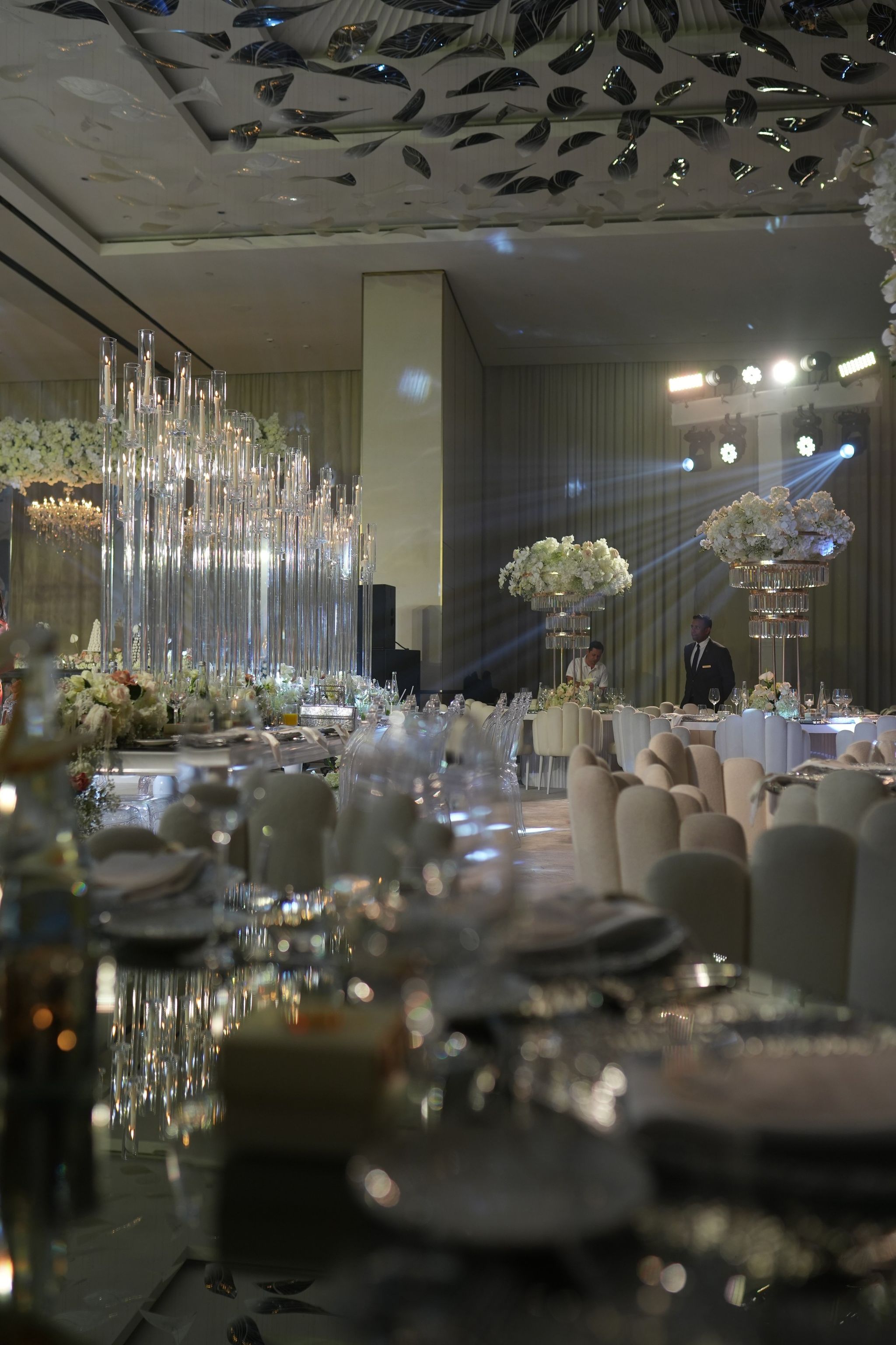Evening view across mirrored tables to glass candelabra and raised ivory floral arrangements