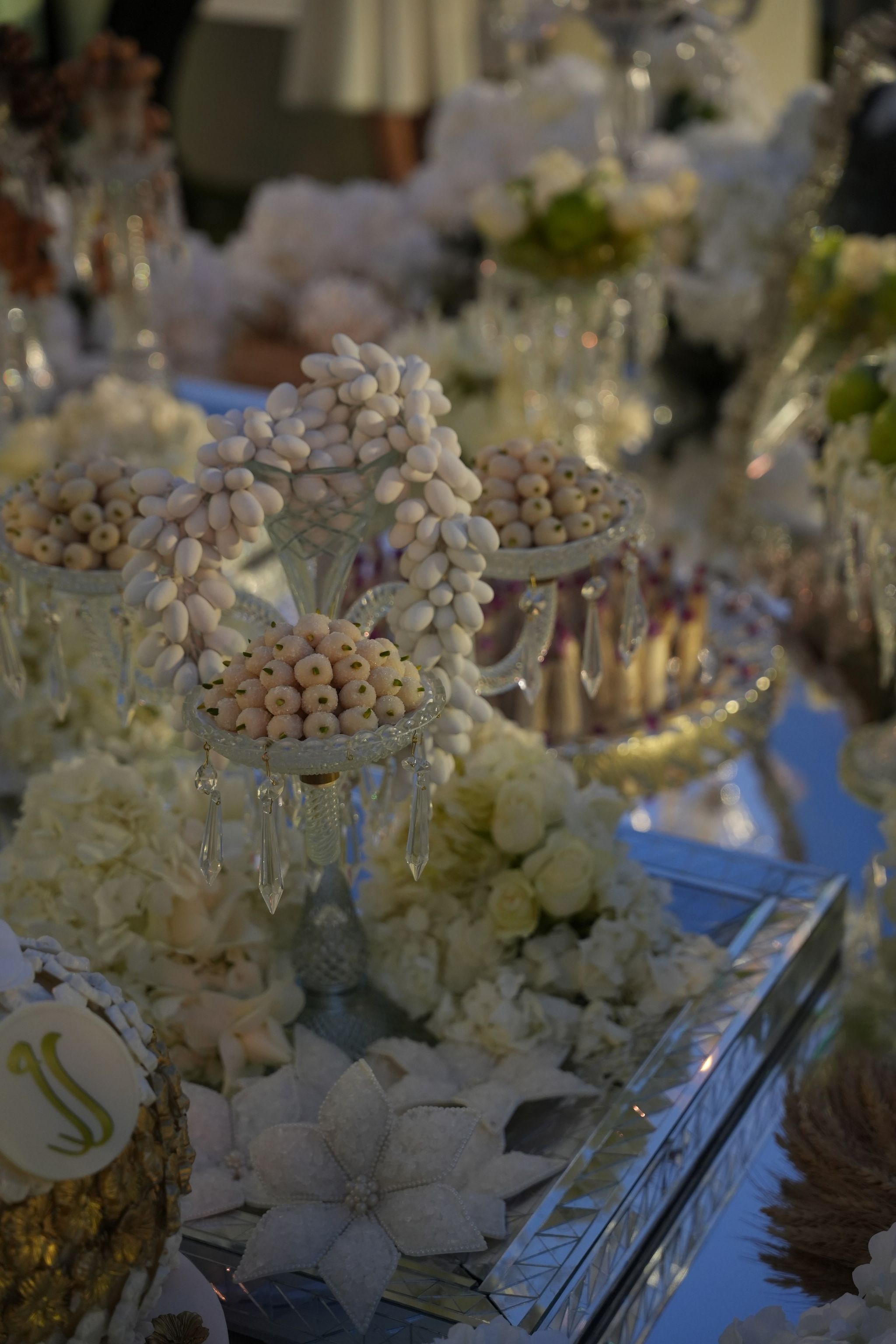 Crystal candelabrum hung with strands of sugared almonds above dishes of sweets and ivory roses