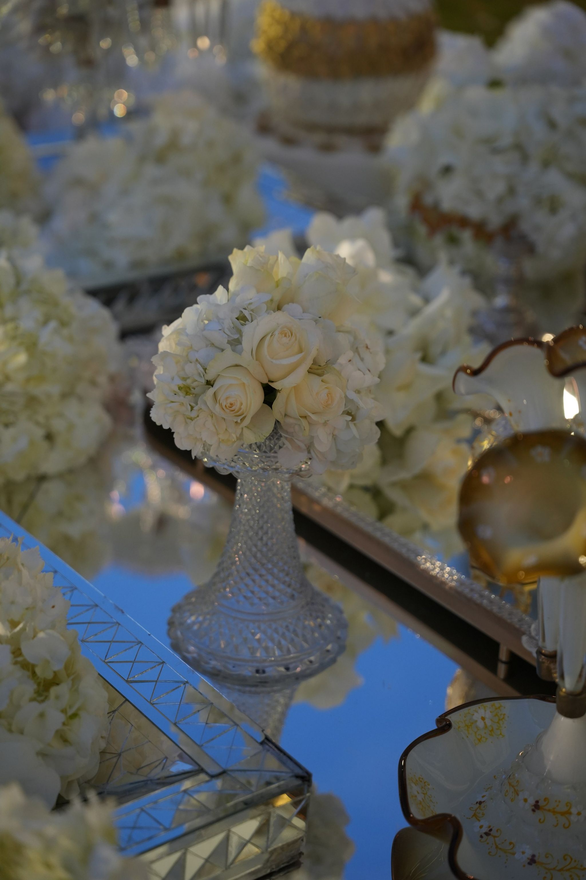 Small posy of ivory roses and hydrangea in a cut-crystal vase on a mirrored table