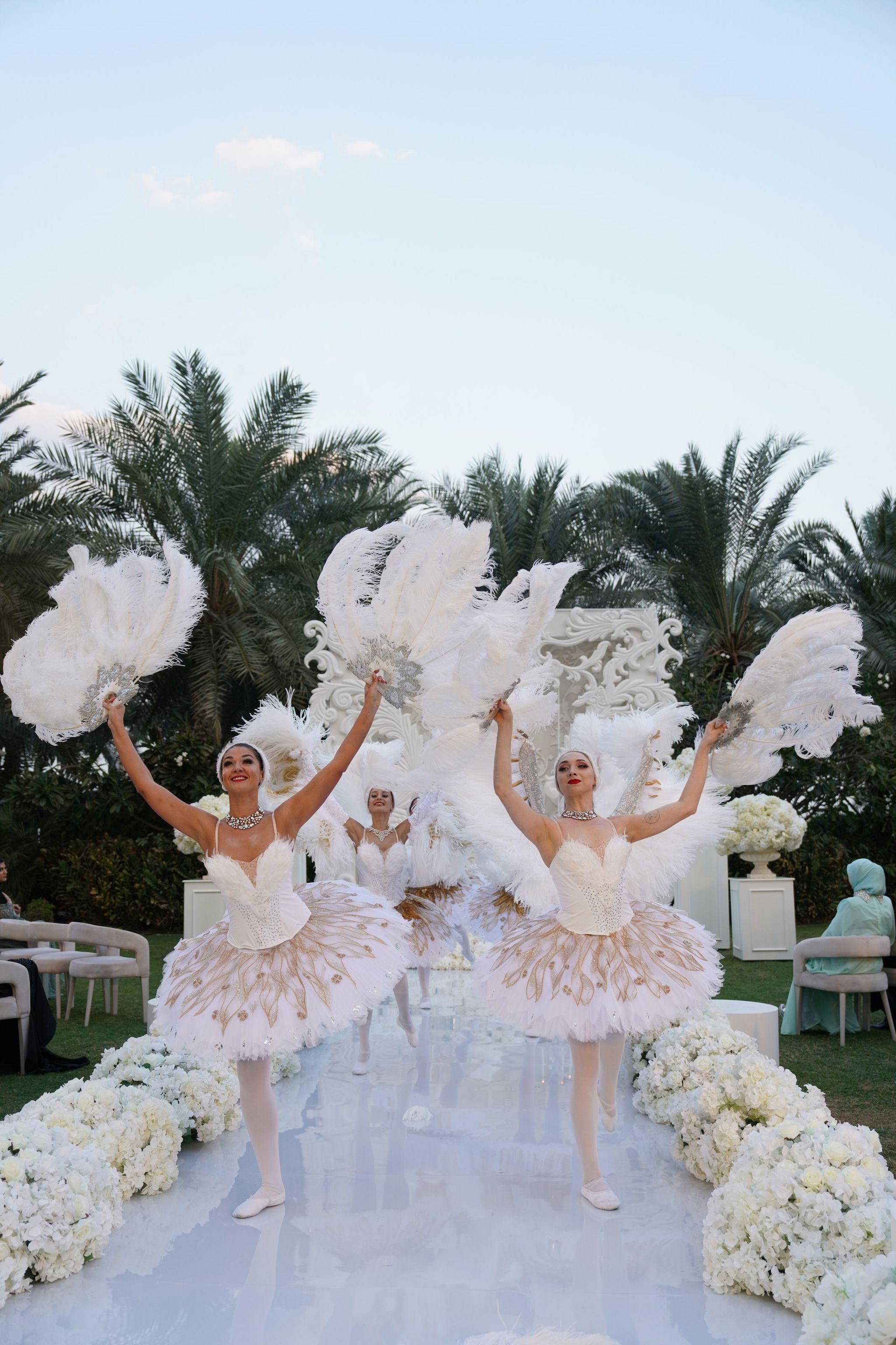 Ballerinas with white feather fans dancing down the mirrored aisle under palms at Raffles The Palm Dubai