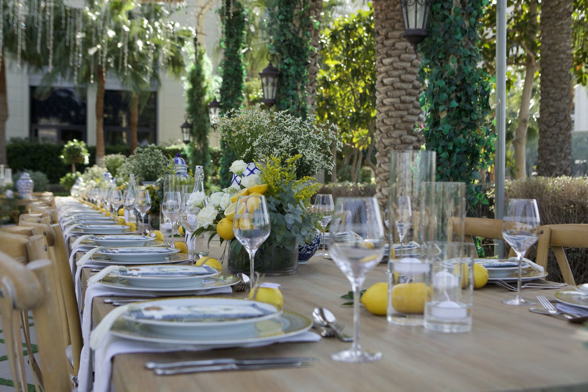 Eye-level view along the long table, lemons and porcelain ginger jars beneath ivy-wrapped palms