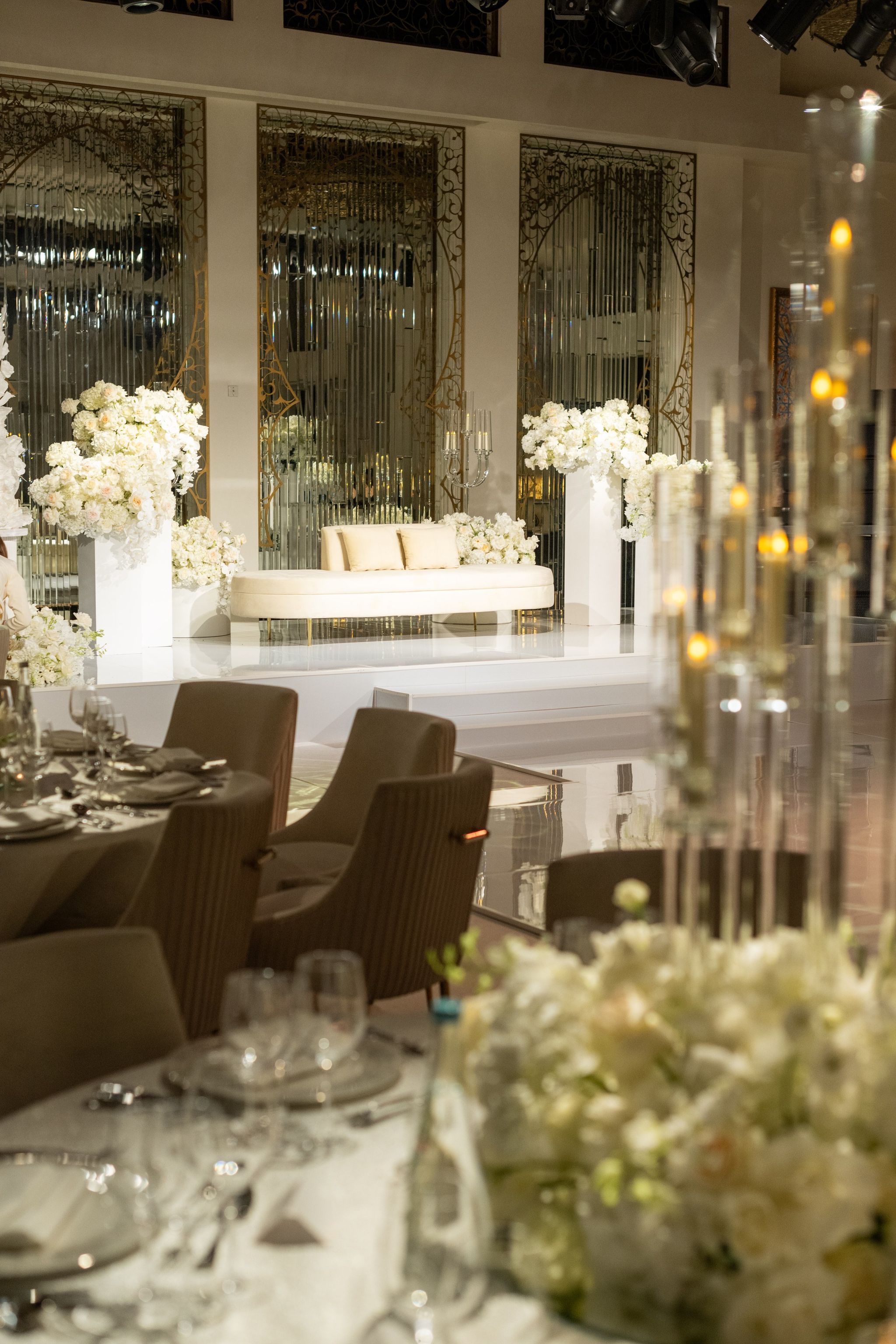 Reception tables and candlelit centrepieces facing the mirrored stage and white loveseat