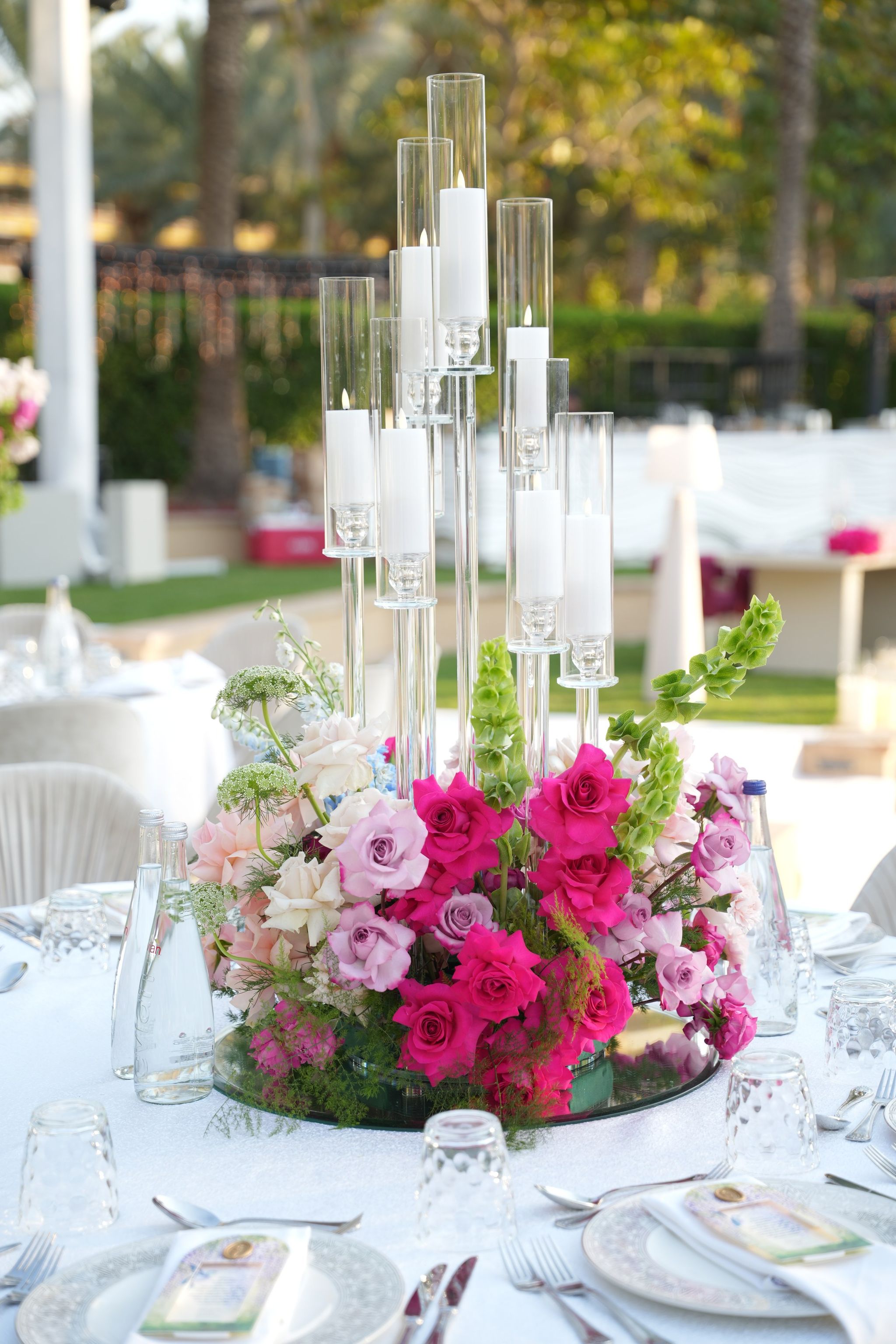 Mirrored centrepiece of fuchsia and lavender roses beneath clustered glass candle columns