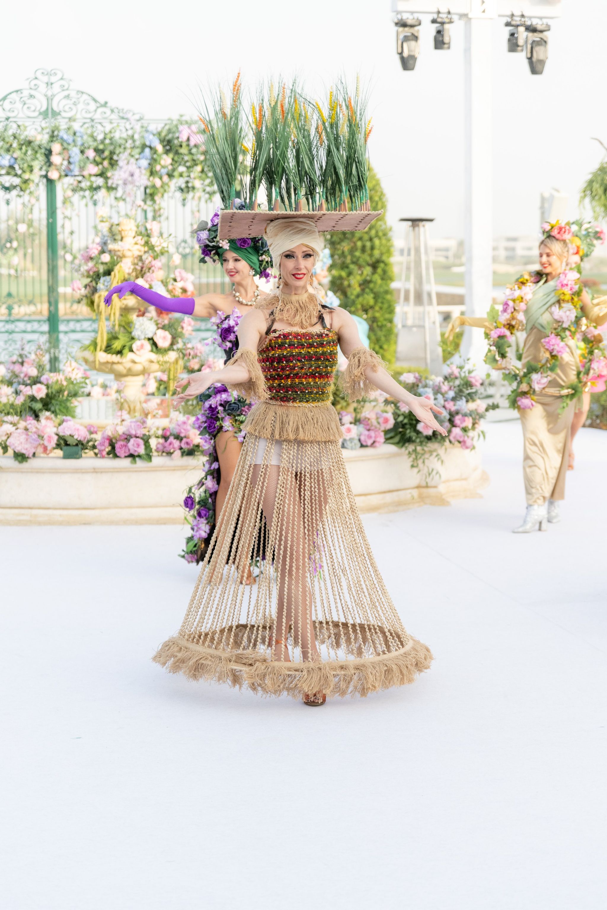 Performer balancing a tray of wheat grass on her head in a fringed beaded gown