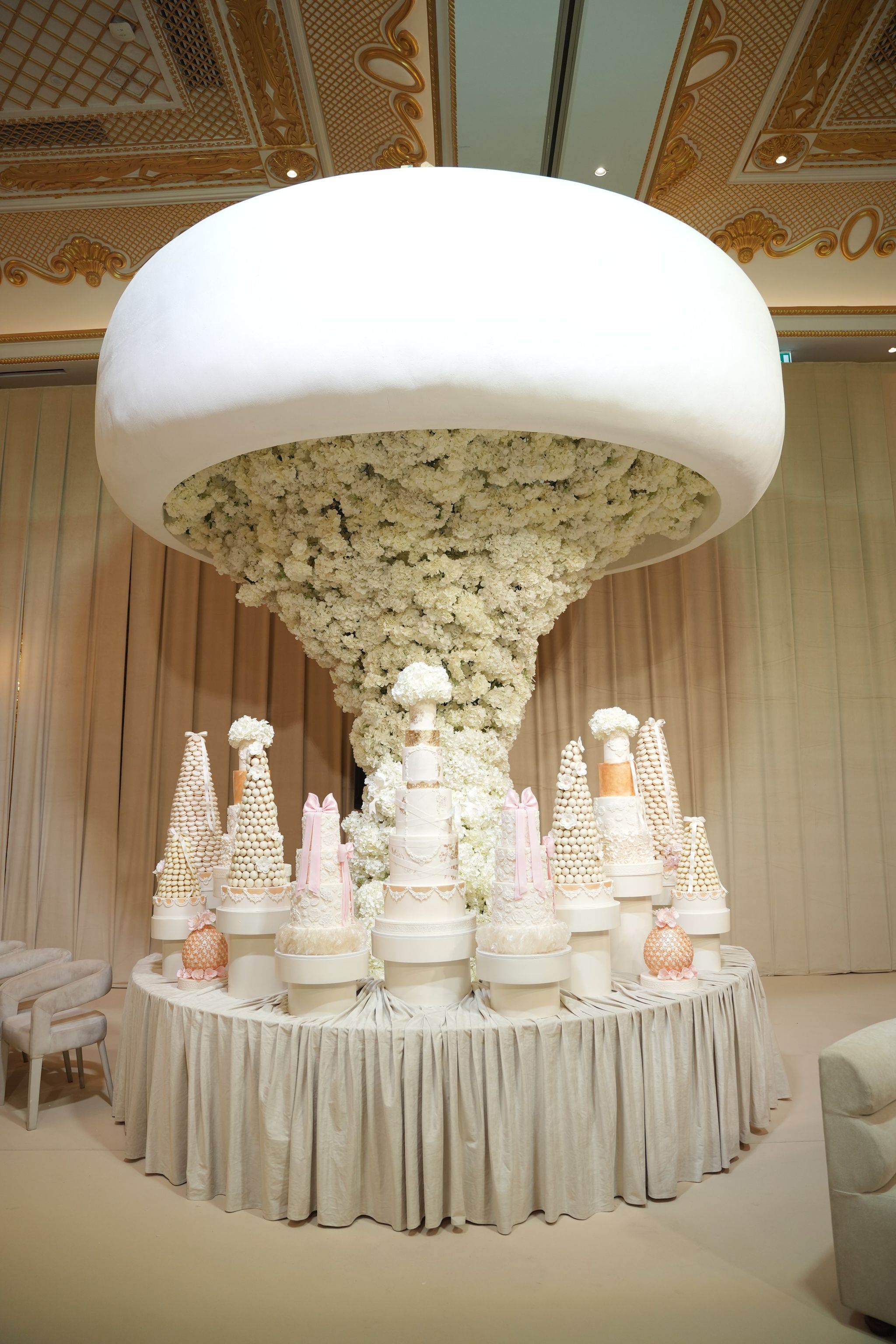 Floral cake installation with croquembouches and tiered cakes under a gilded ceiling at Raffles The Palm Dubai