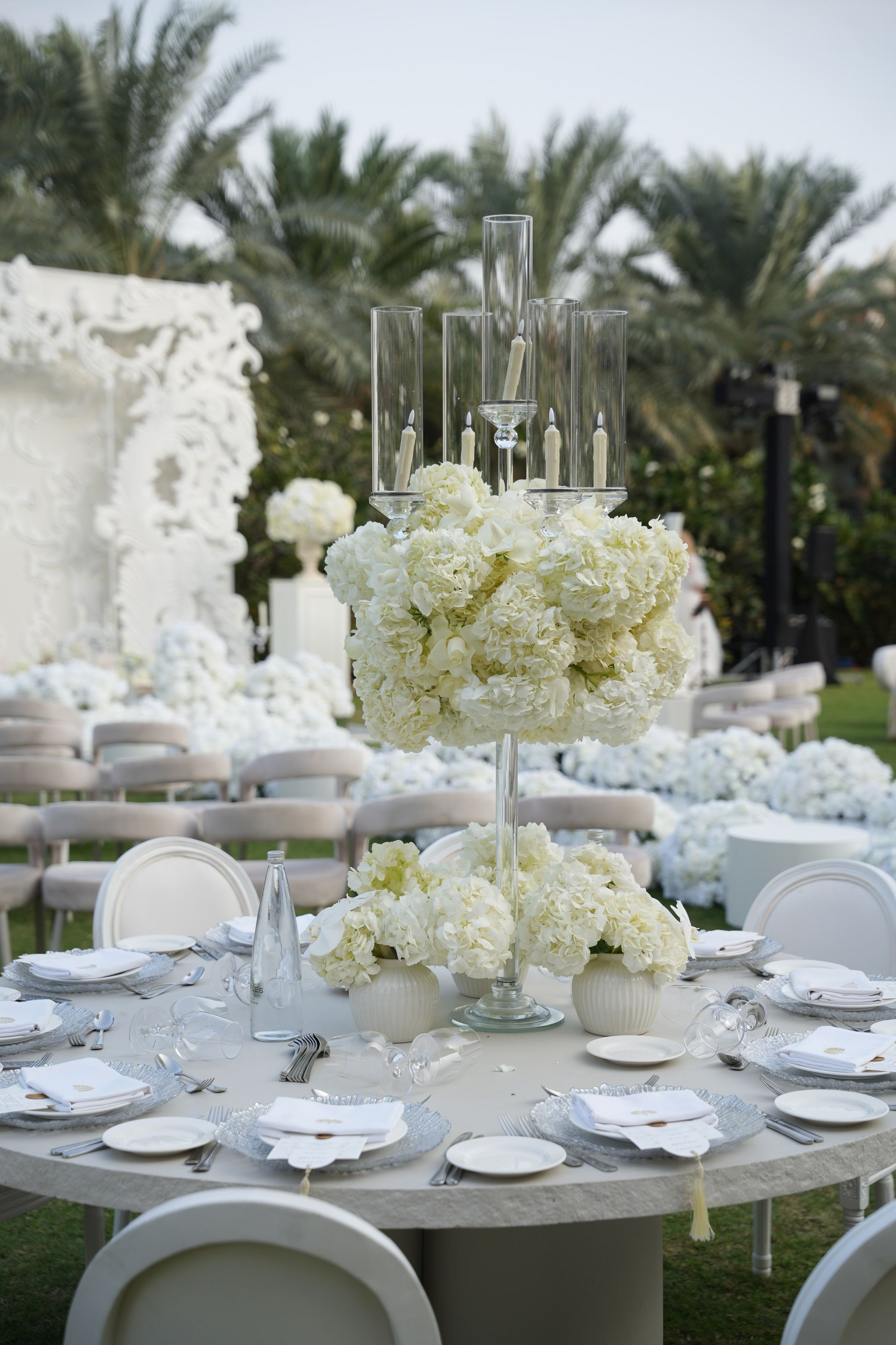 Tall glass candle holders rising above a white hydrangea centrepiece on a laid round table