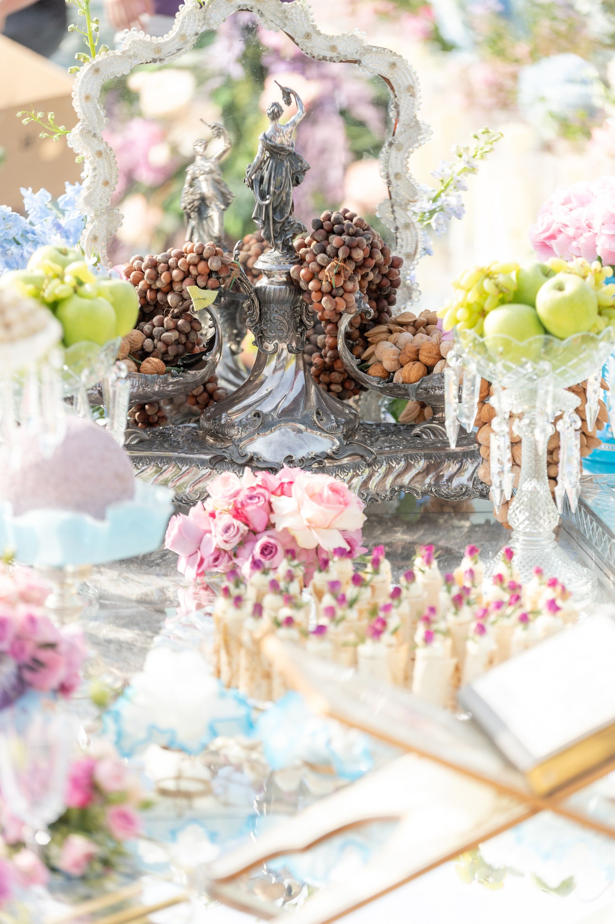 Silver centrepiece of hazelnuts and almonds beside green apples, roses and sugar-tipped sweets