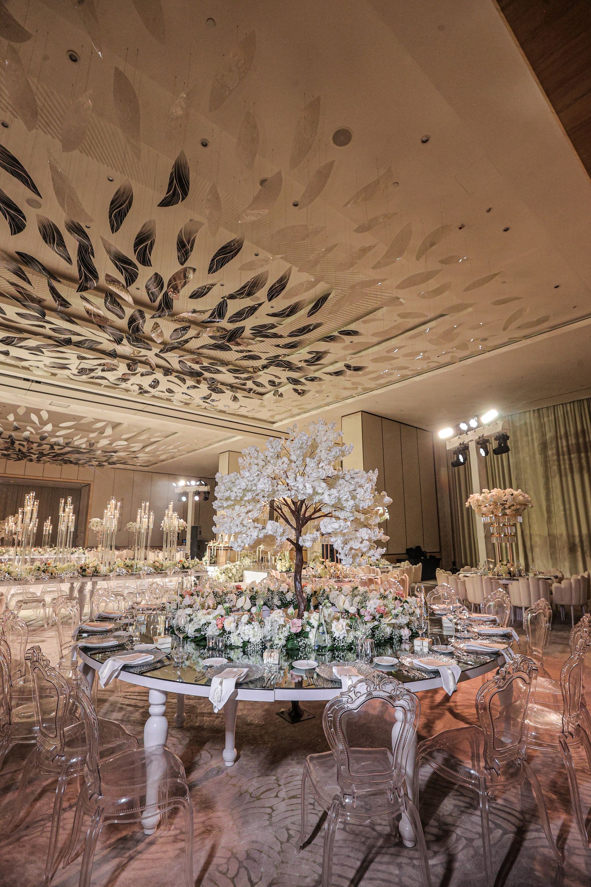 Round mirrored table beneath a white blossom tree, ringed by clear ghost chairs at The St. Regis Dubai, The Palm