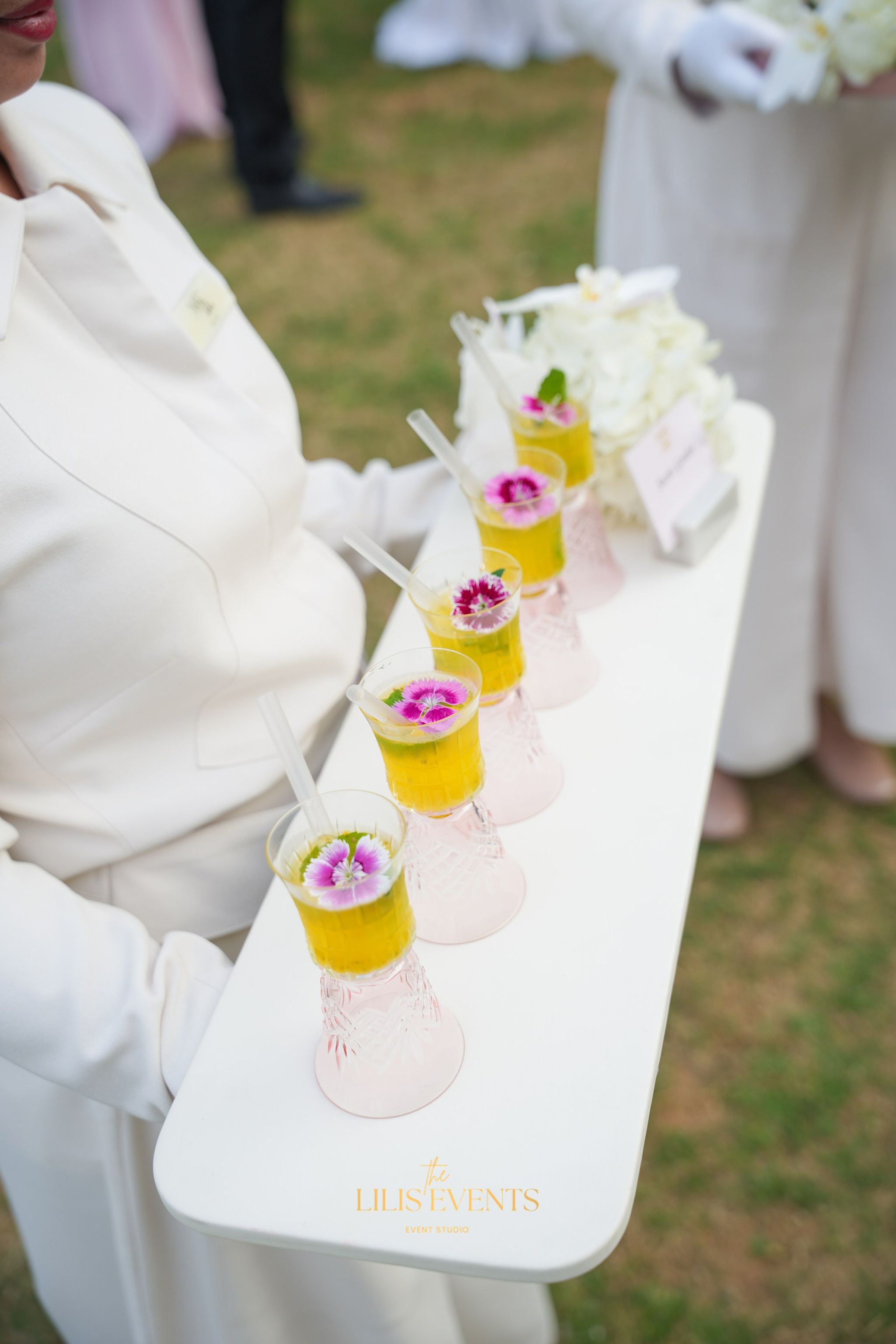 Mango drinks garnished with pink dianthus in etched pink glasses, carried on a white tray