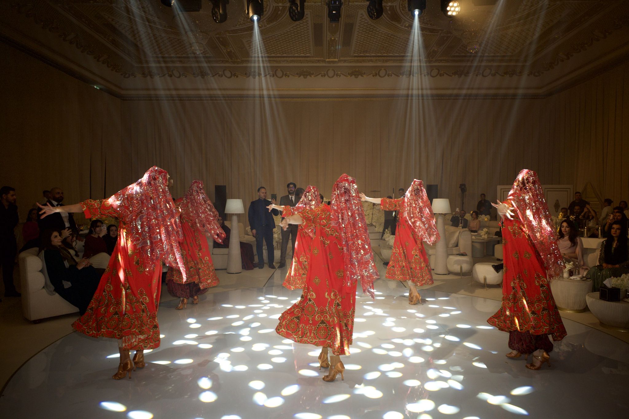 Dancers in red embroidered gowns and sequinned veils performing on a lit dance floor
