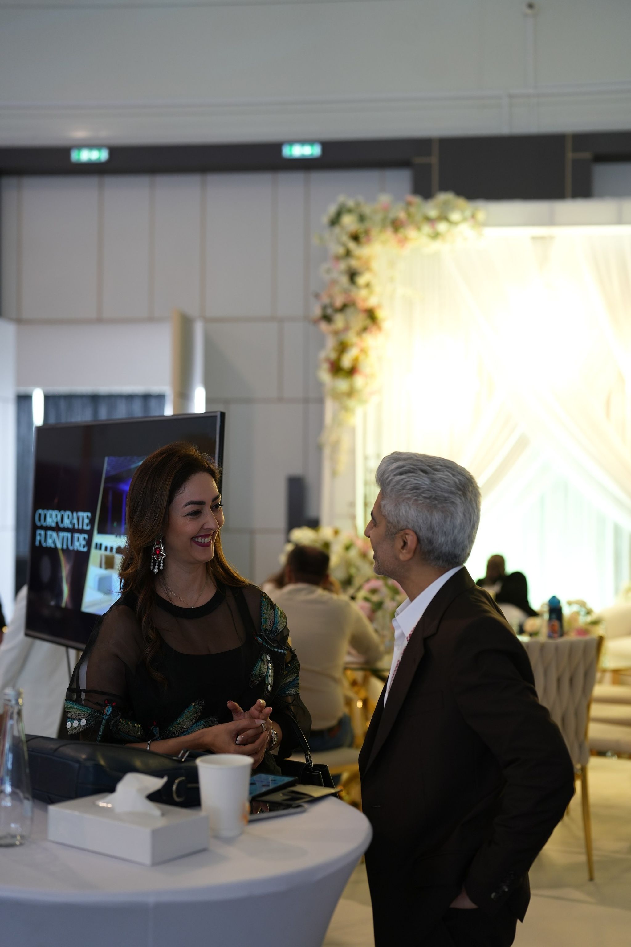 Conversation by a round table, with a floral arch and draped backdrop in the exhibition hall