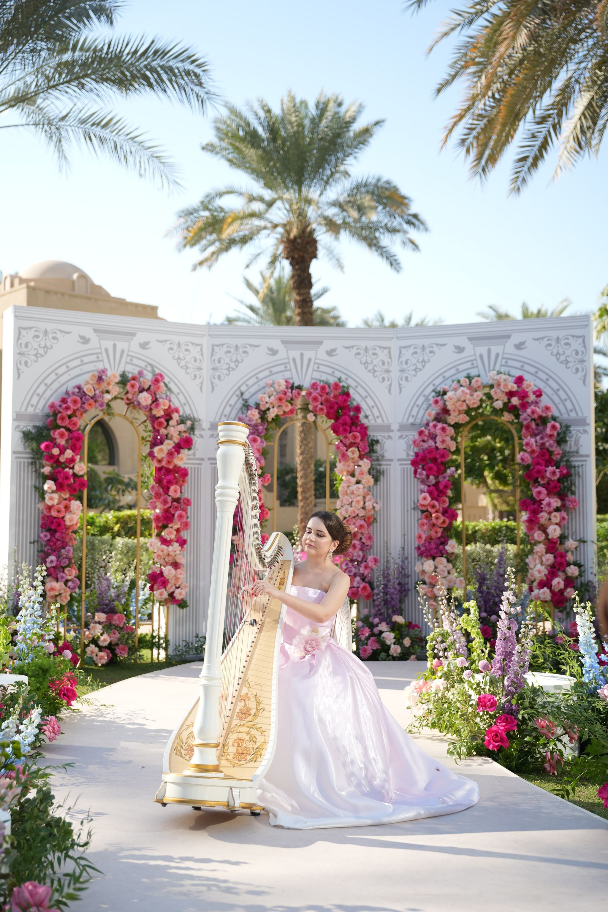 Harpist in a lilac gown at the head of the aisle beneath three rose arches