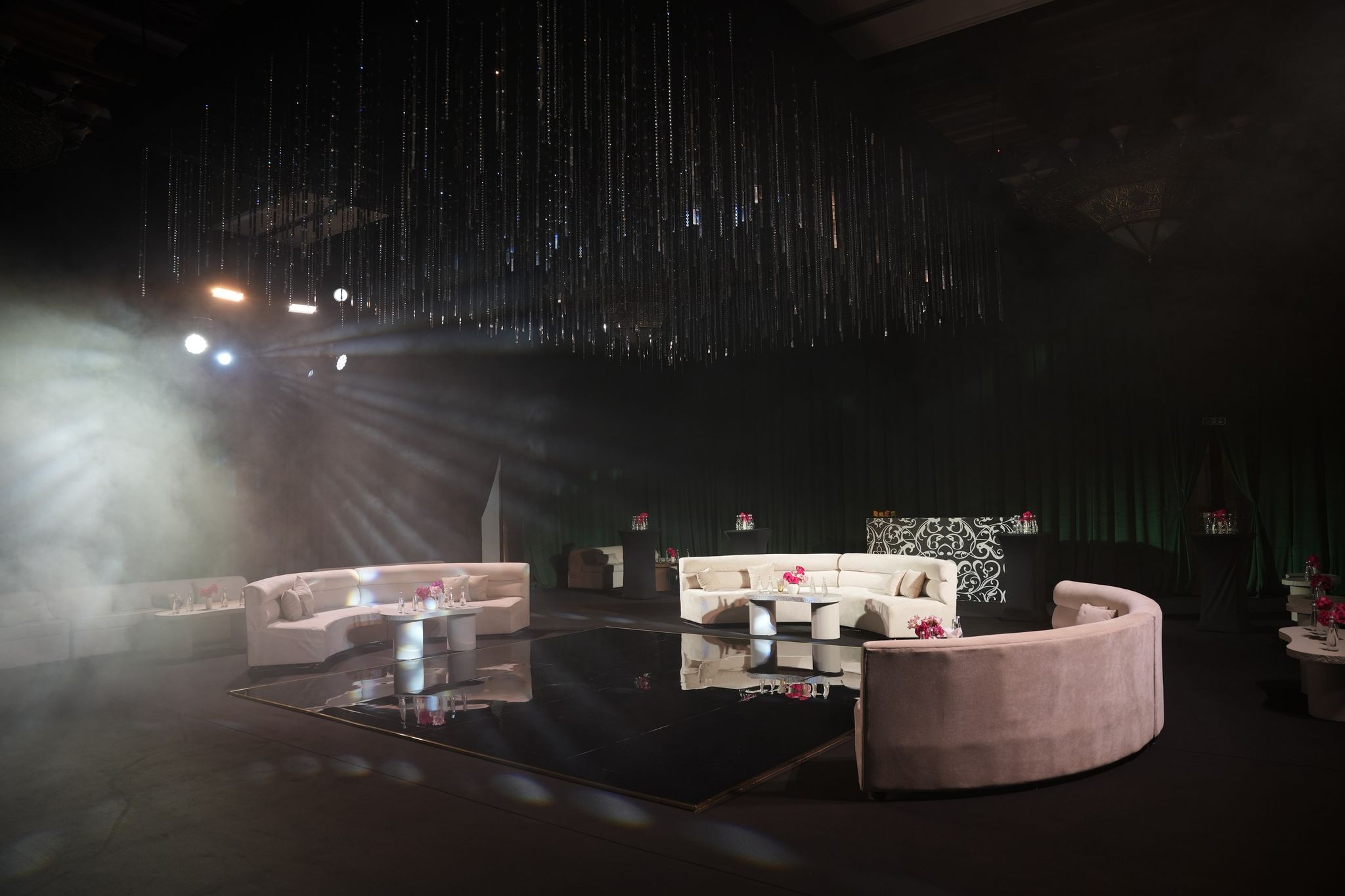 Haze-lit lounge with ivory and blush sofas beneath a canopy of hanging crystal strands