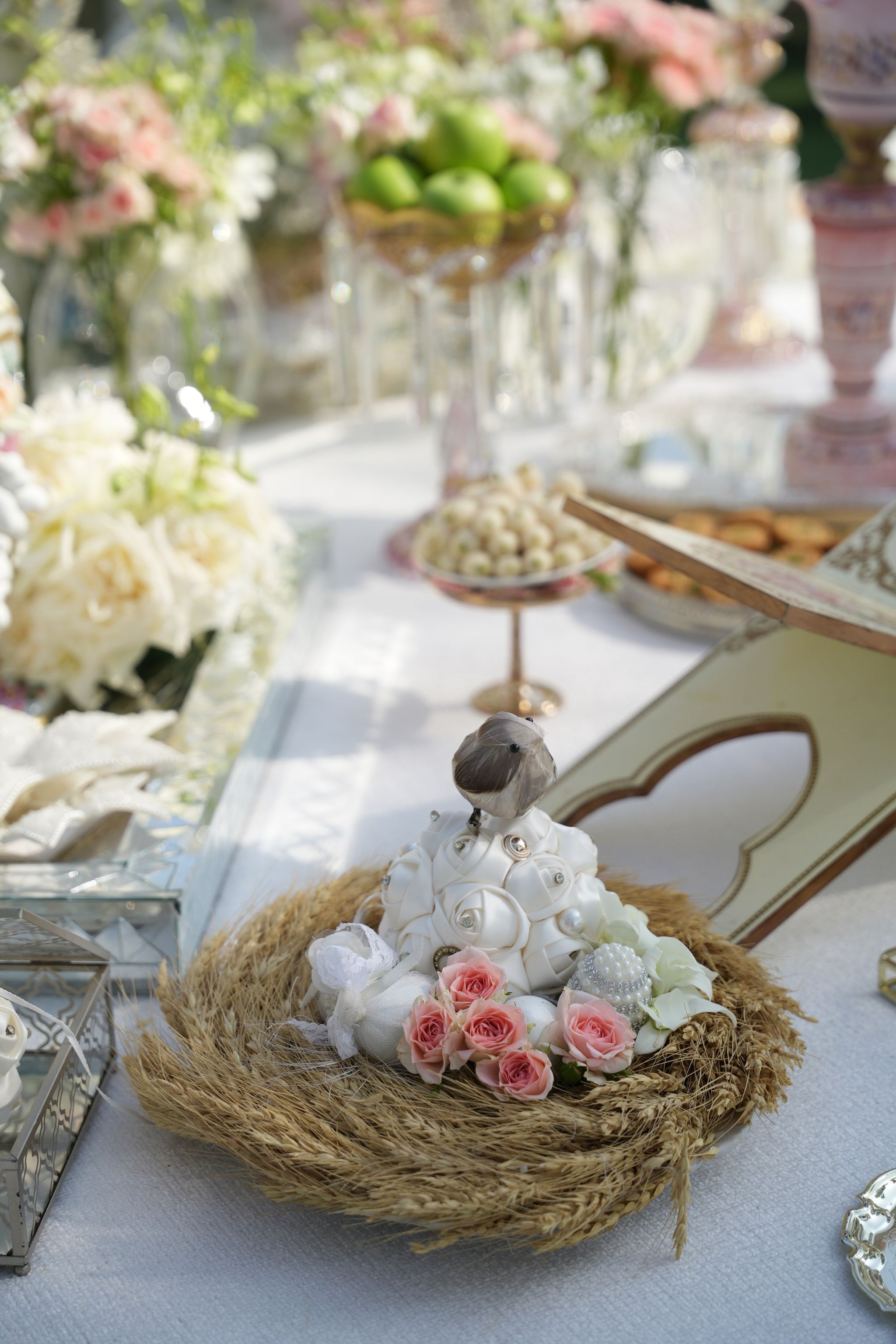 Woven wheat nest holding white sugared shells, a bird figurine and pink spray roses